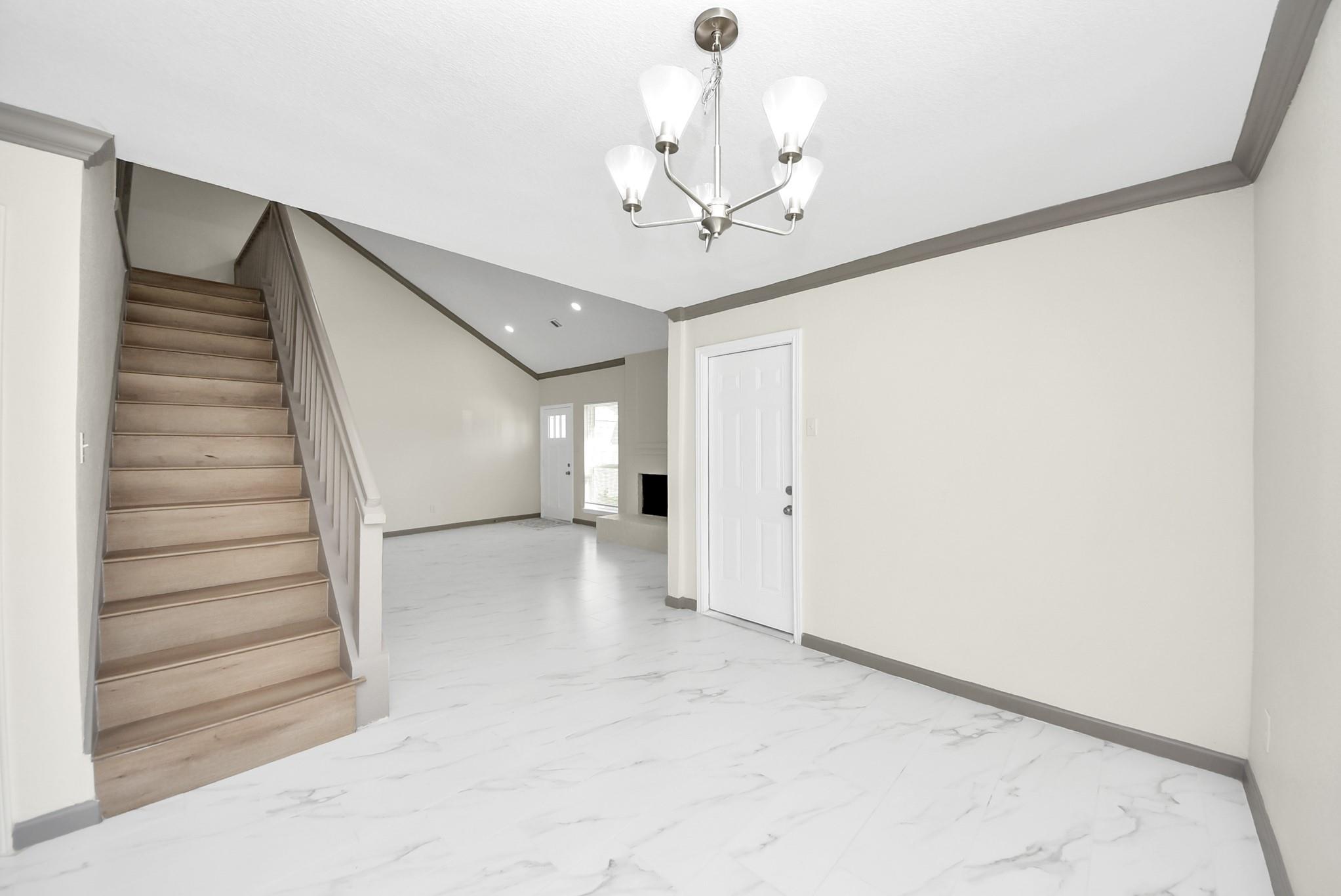 Empty entry and living area with a wood staircase and white veined tile flooring.
