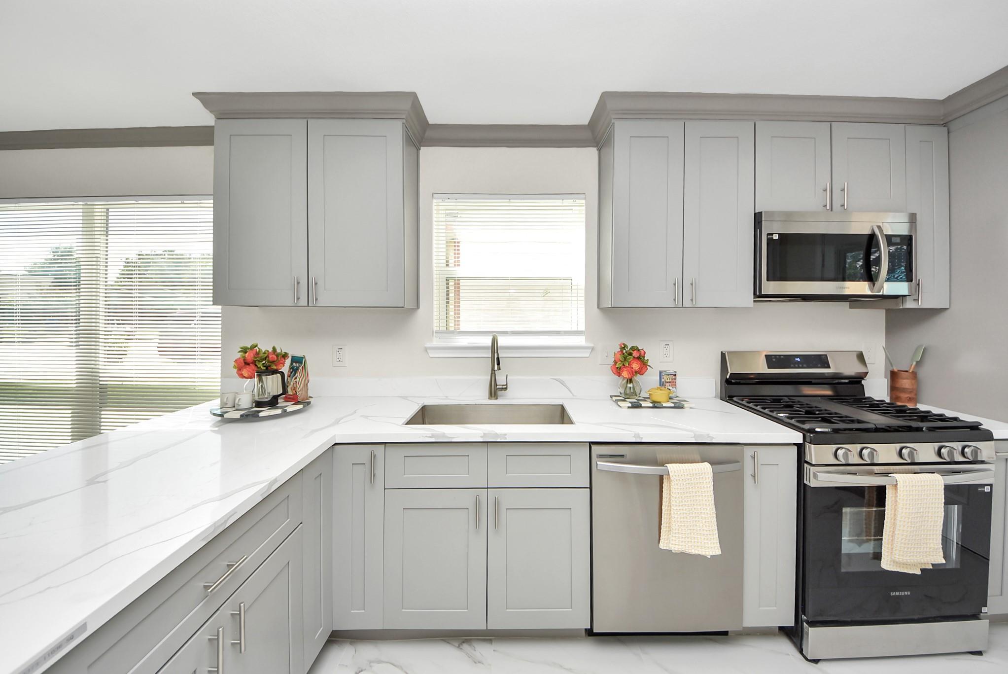 Kitchen with gray shaker cabinets, white veined countertops, and stainless steel gas range.