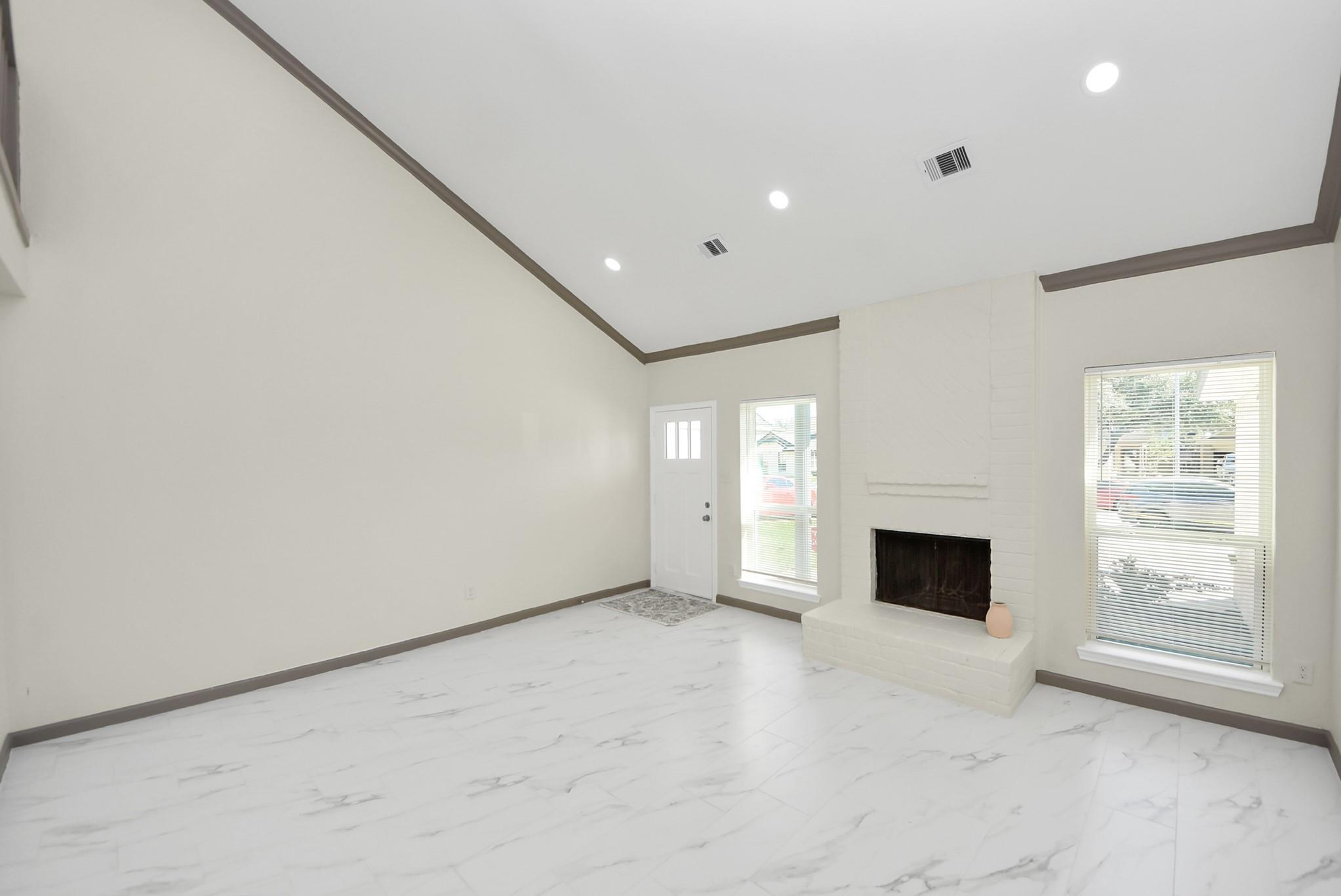 Empty living room with marble-look tile floors, a white brick fireplace, and tall windows.
