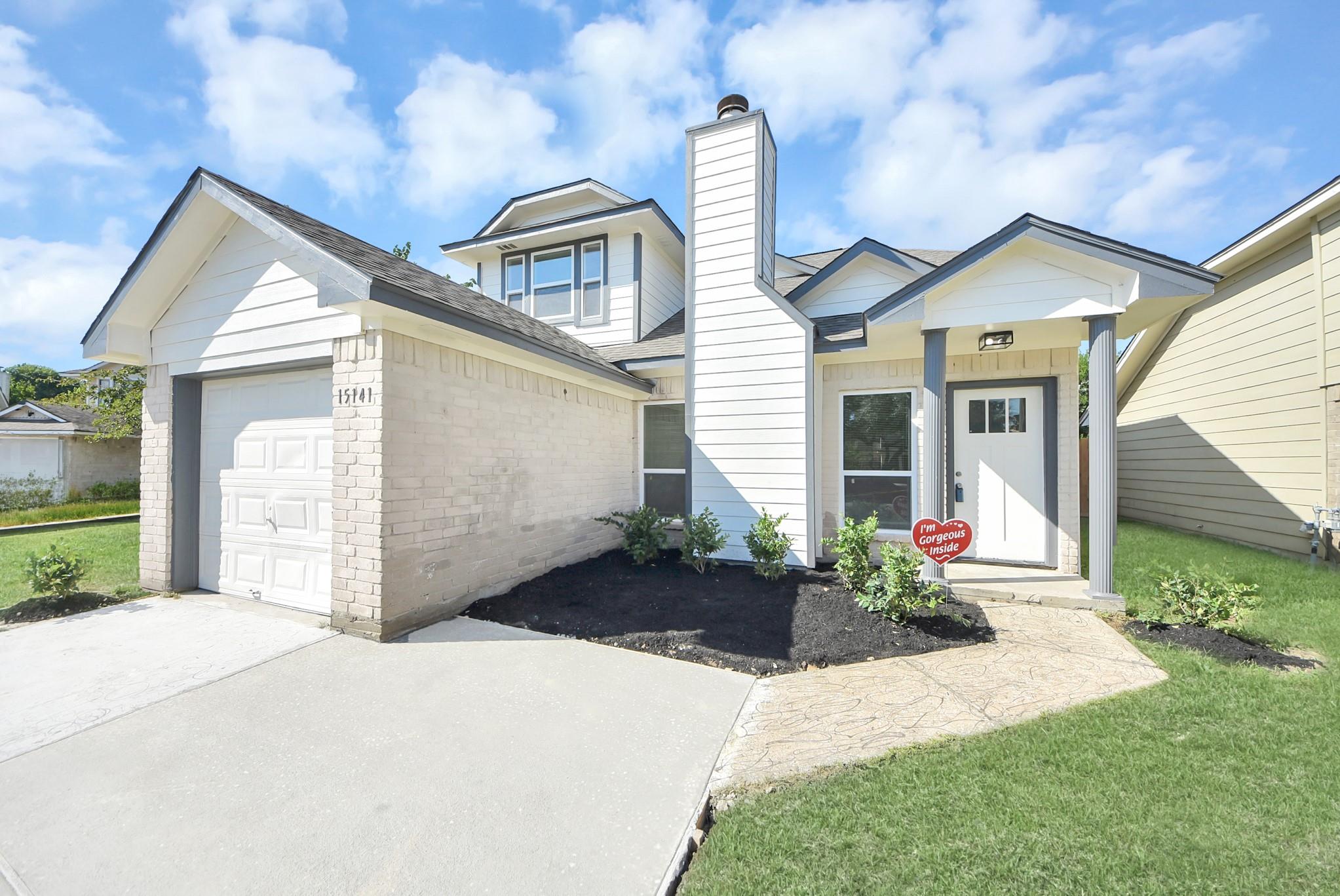 Two-story white and brick home with an attached garage, covered entry, and landscaped front garden.