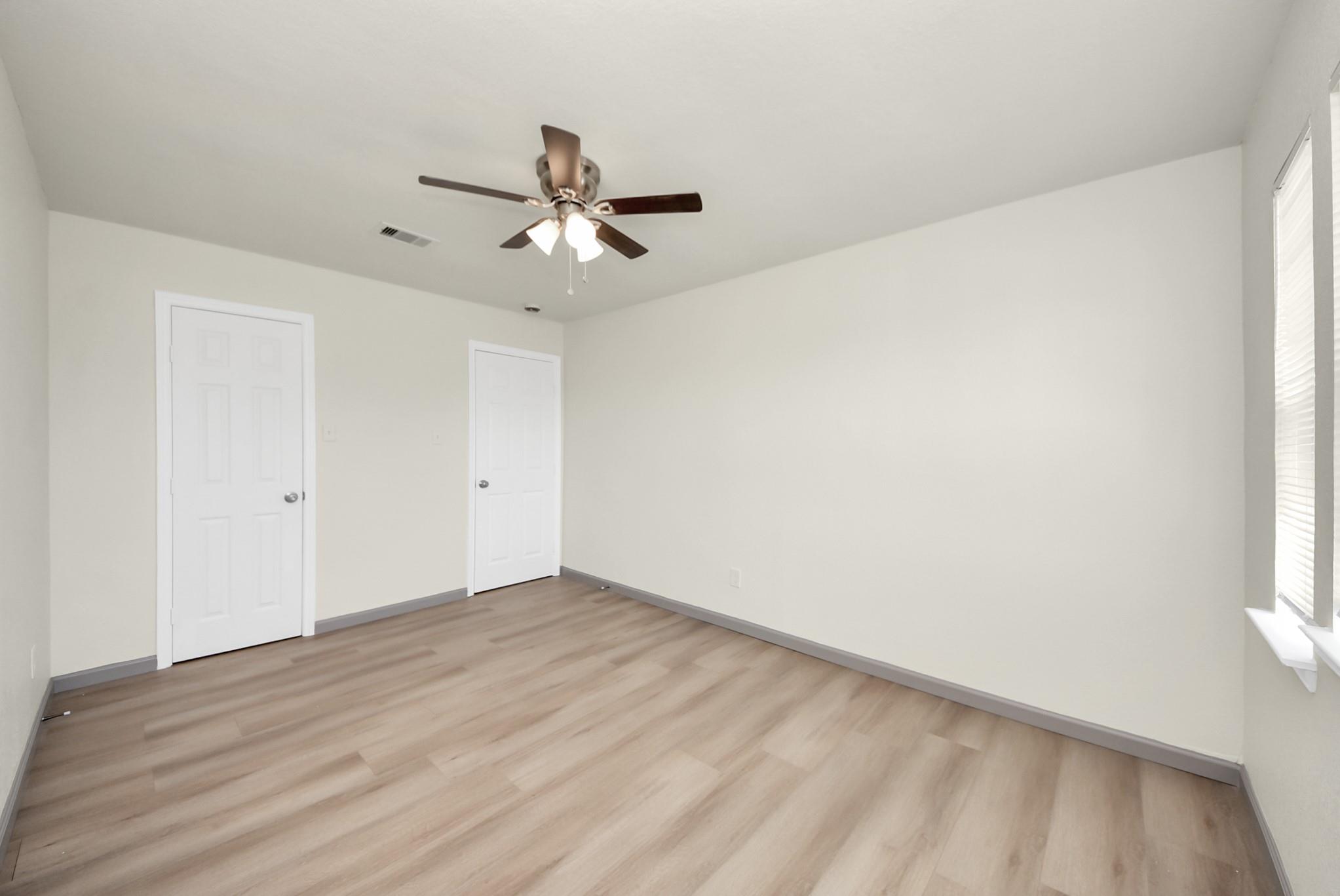 Empty bedroom with light wood-look floors, two doors, and a ceiling fan with lights.