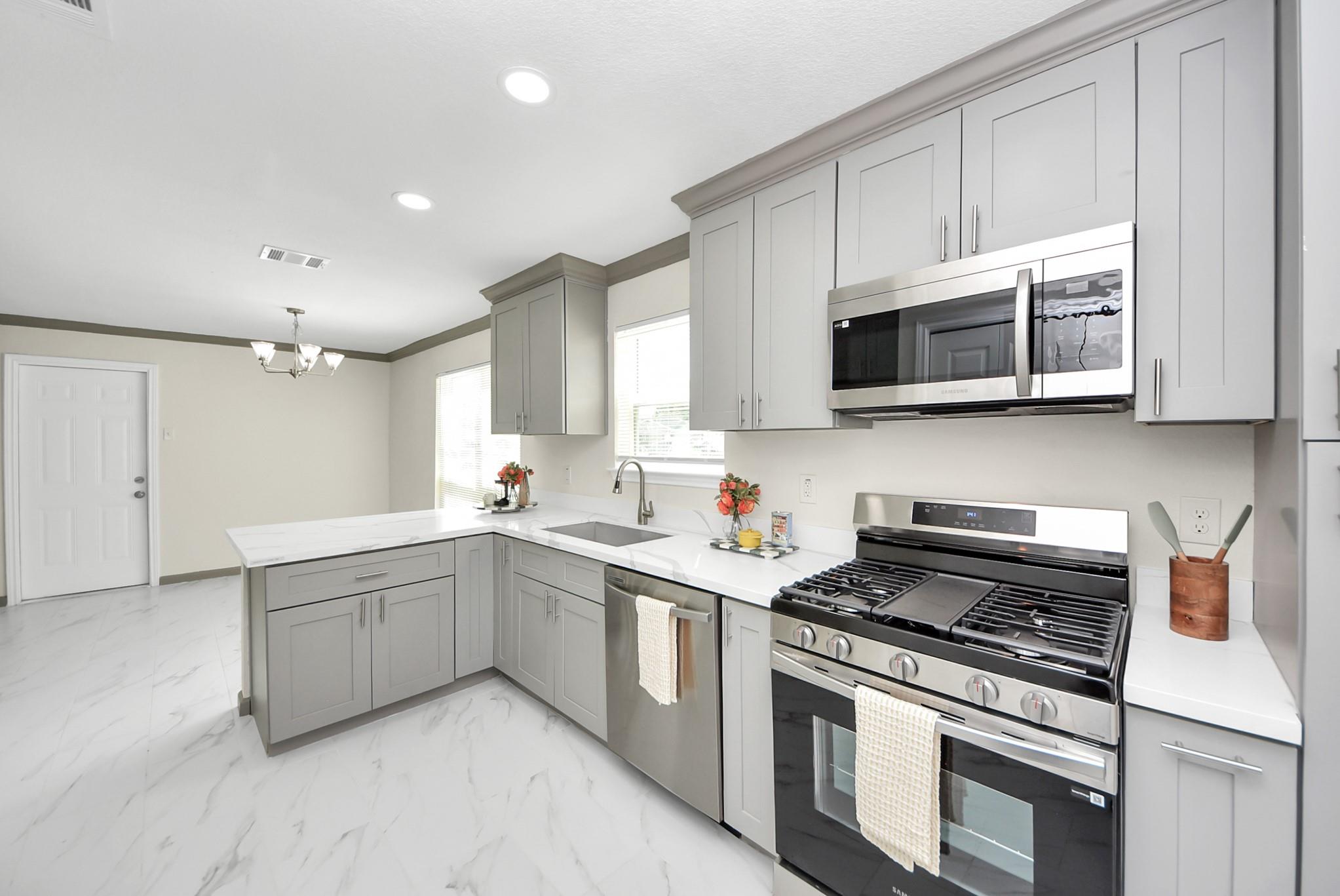 Bright kitchen with gray cabinets, white counters, an island, and a stainless steel gas range.