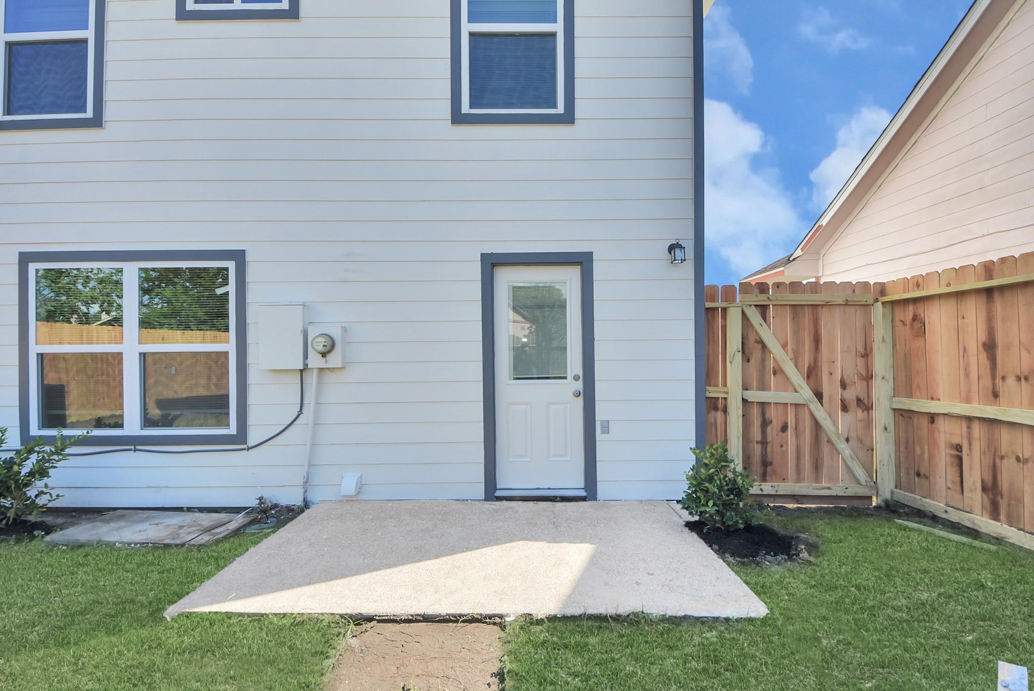 House’s rear patio and door beside a wooden privacy fence and grassy yard.
