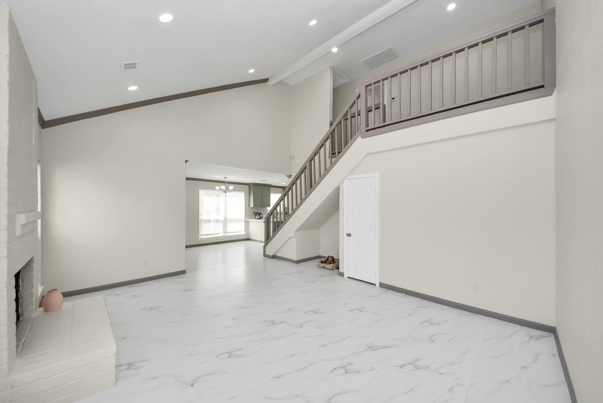 Living room with a white brick fireplace, marble-look tile, and staircase to an open landing.