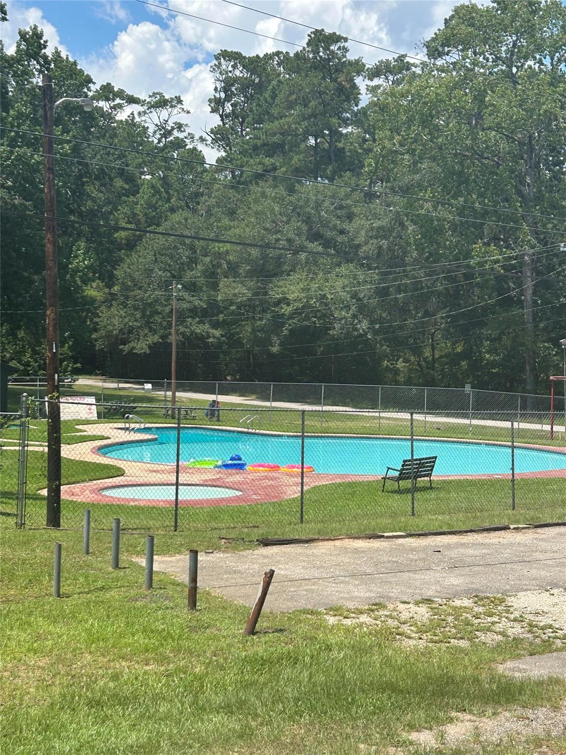 Fenced outdoor swimming pool with a small shallow pool, colorful floats, and mature trees.