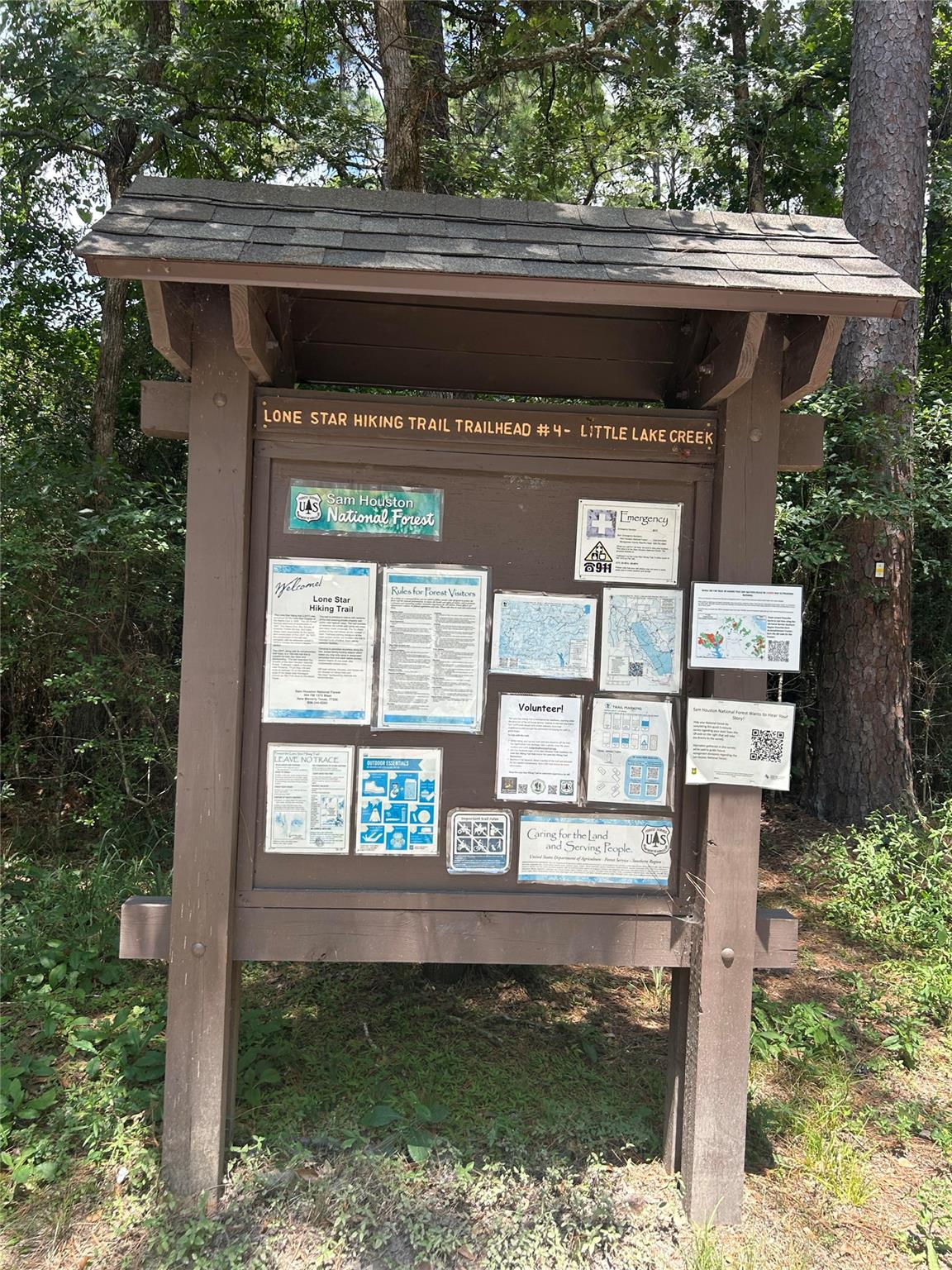 Lone Star Hiking Trail Trailhead #4 kiosk with maps and visitor notices beneath a shingled roof in the forest.