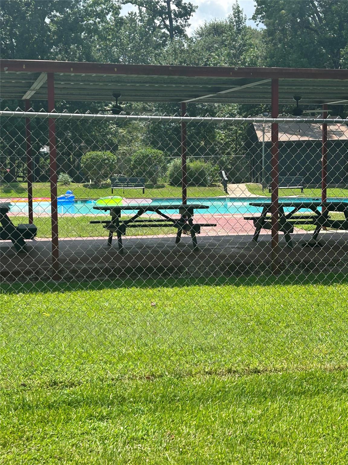 Outdoor swimming pool with a covered pavilion, picnic tables, and surrounding trees.