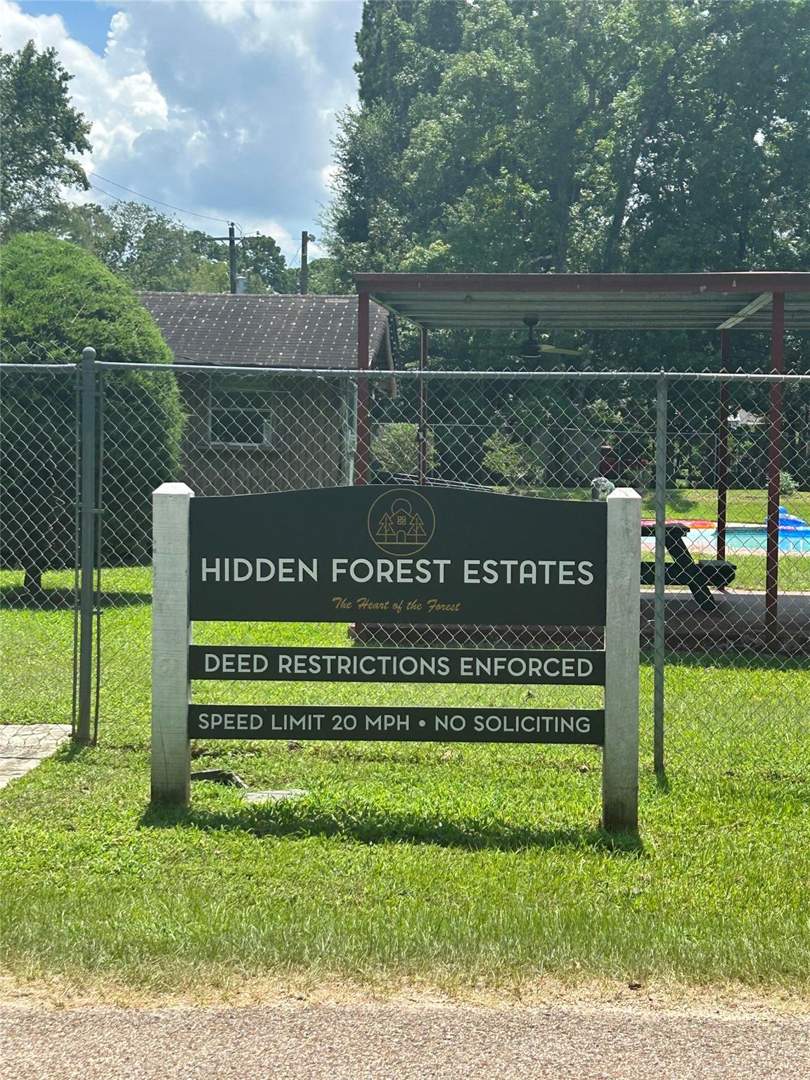 Hidden Forest Estates entrance sign beside a fenced swimming pool and covered patio.