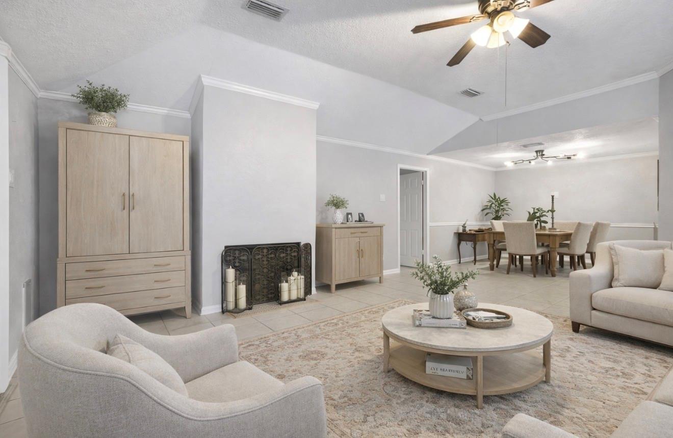 Living room with neutral seating, a round coffee table, and an adjoining dining area beneath a high ceiling.