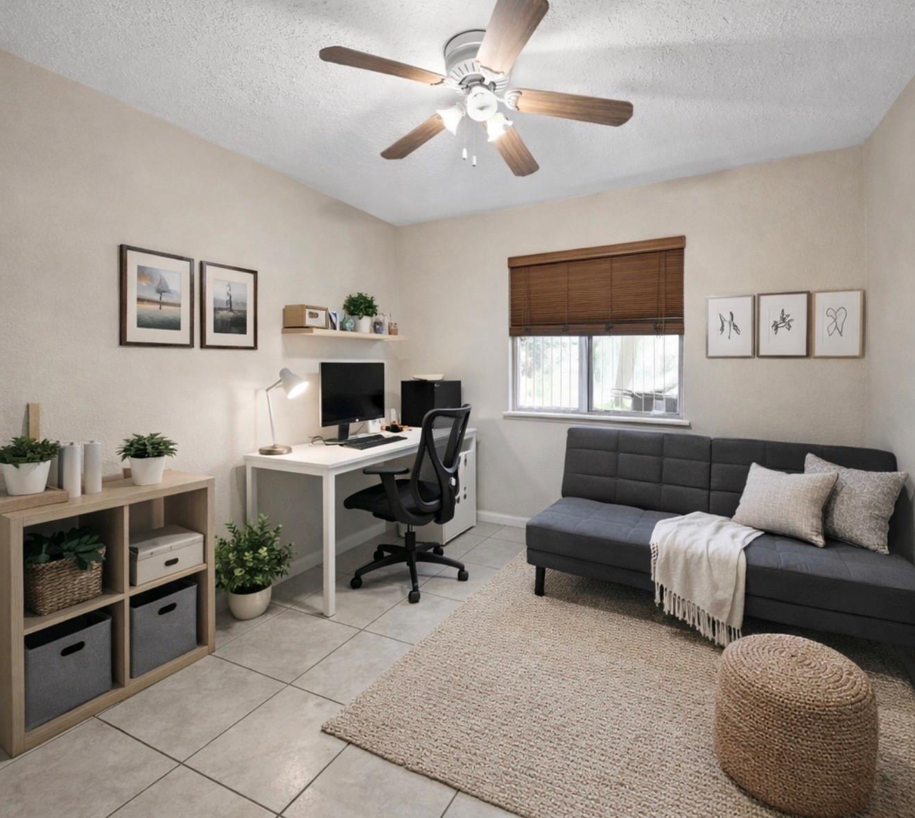 Home office with a white computer desk, gray sofa, tiled floor, and ceiling fan.