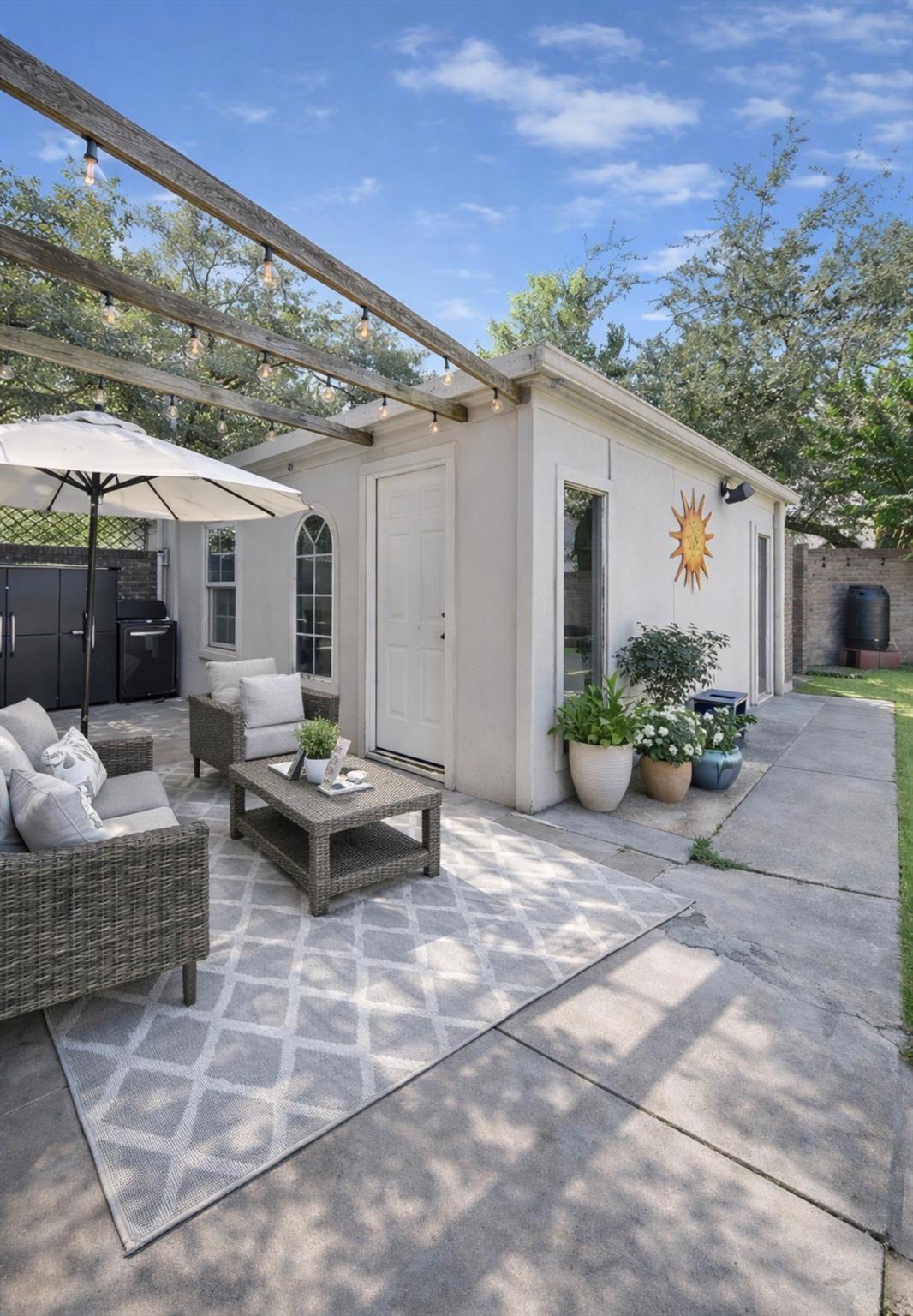 Backyard patio with wicker seating, a white outbuilding, and a pergola with string lights.