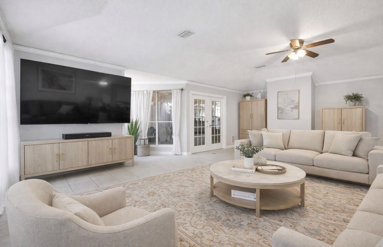 Furnished living room with a large wall-mounted television, pale sectional, and French doors.
