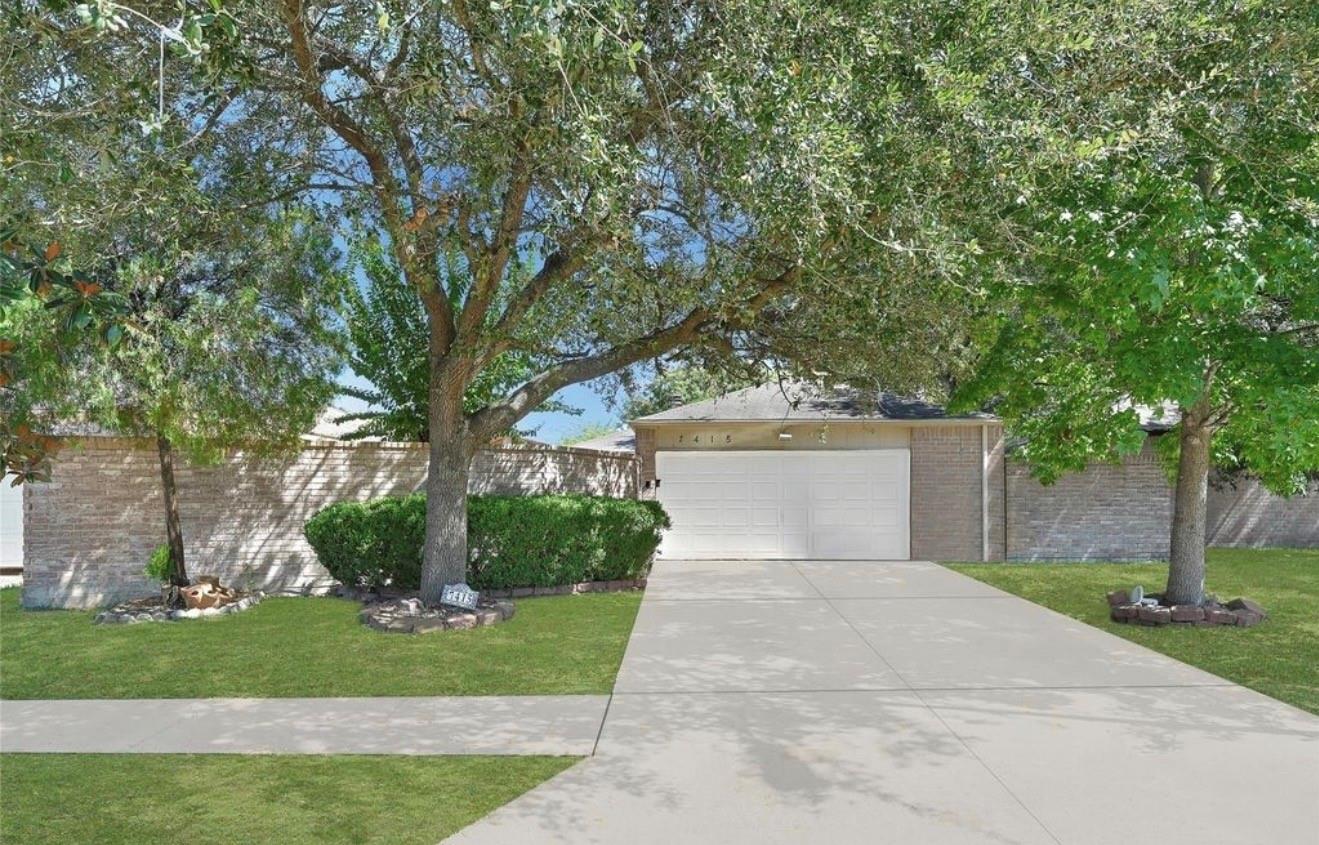 Single-story brick home behind mature trees, with a wide driveway and white double garage.