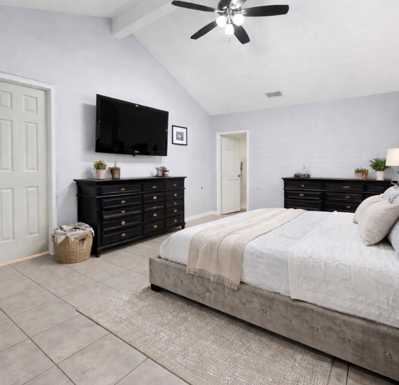 Furnished bedroom with a large bed, black dressers, and a wall-mounted television.