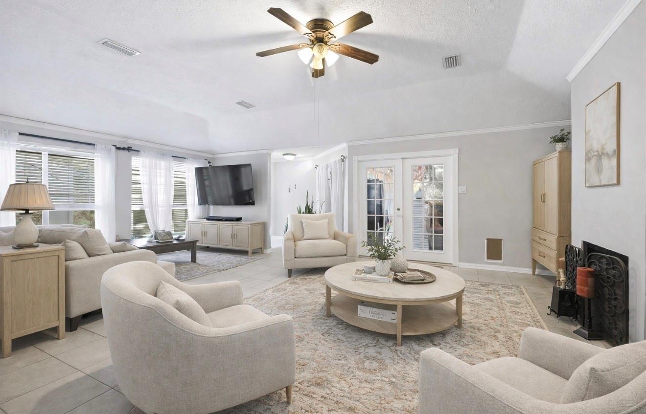 Bright living room with a ceiling fan, large curtained windows, French doors, and a fireplace.
