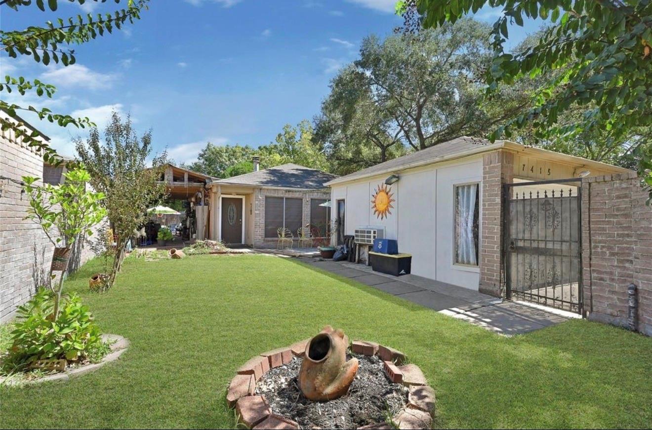 Single-story home behind a green backyard lawn, with a brick fire pit and gated entrance.