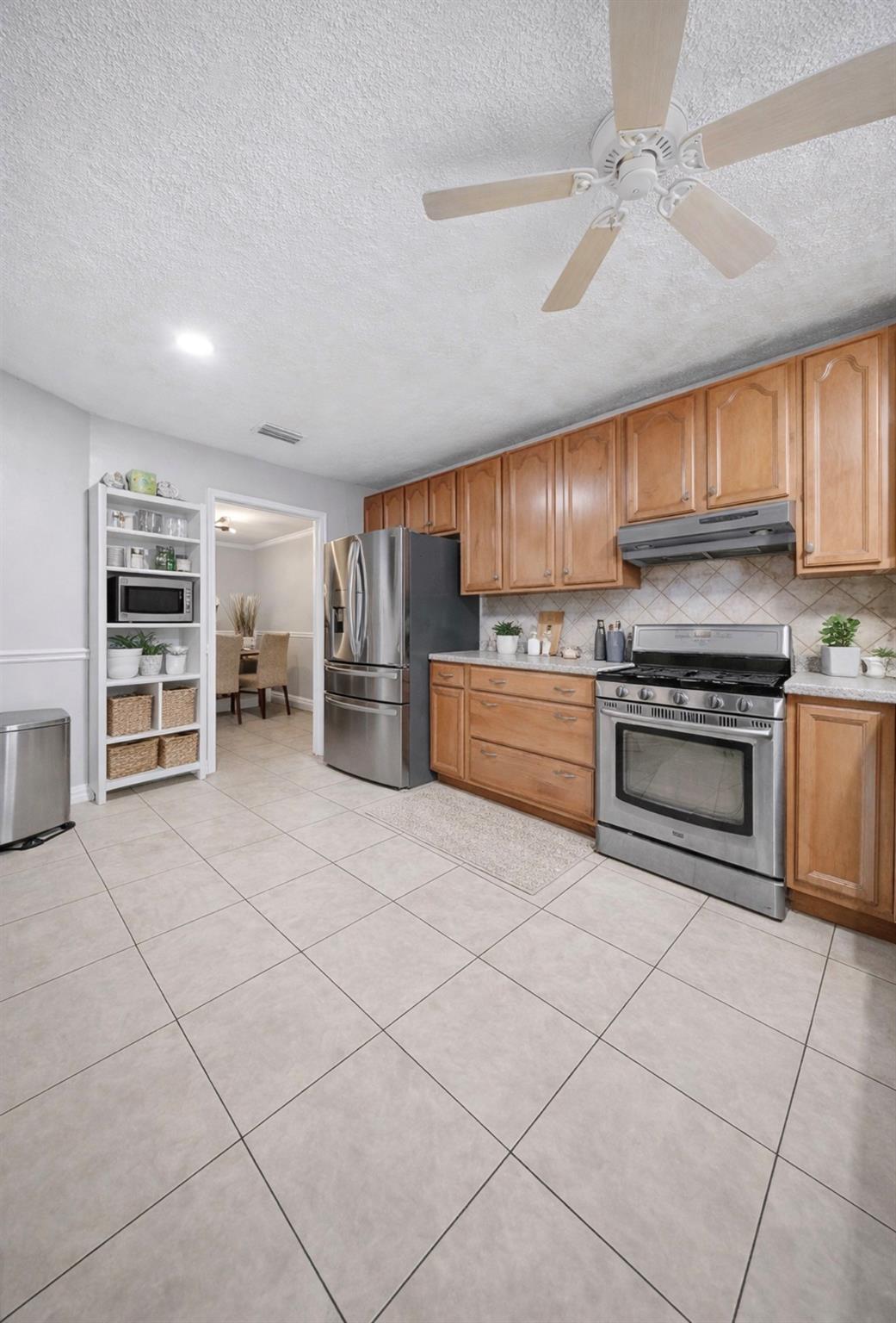 Kitchen with wood cabinets, stainless steel appliances, tile floors, and a ceiling fan.