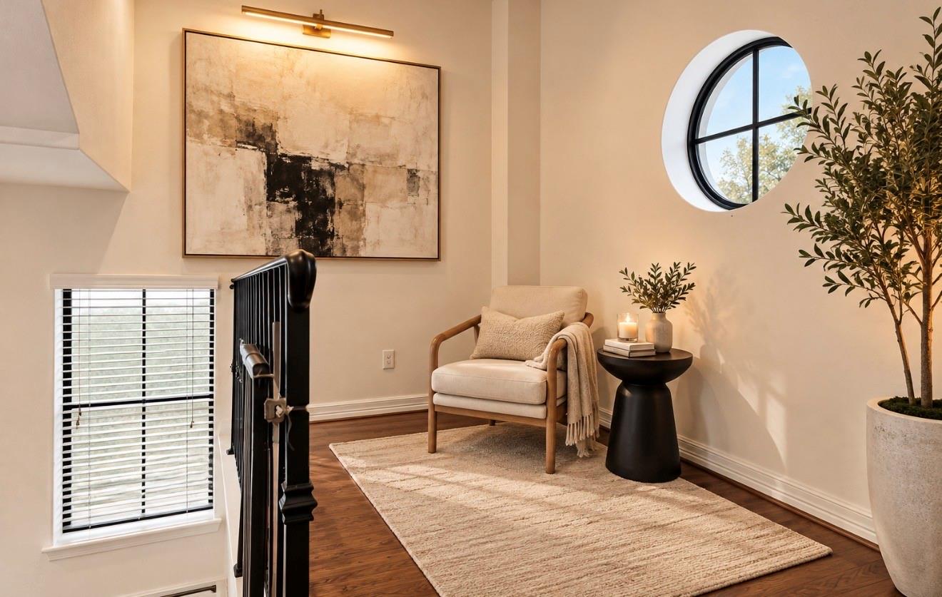 Staged upstairs sitting area with a round window, cream armchair, and dark wood railing.