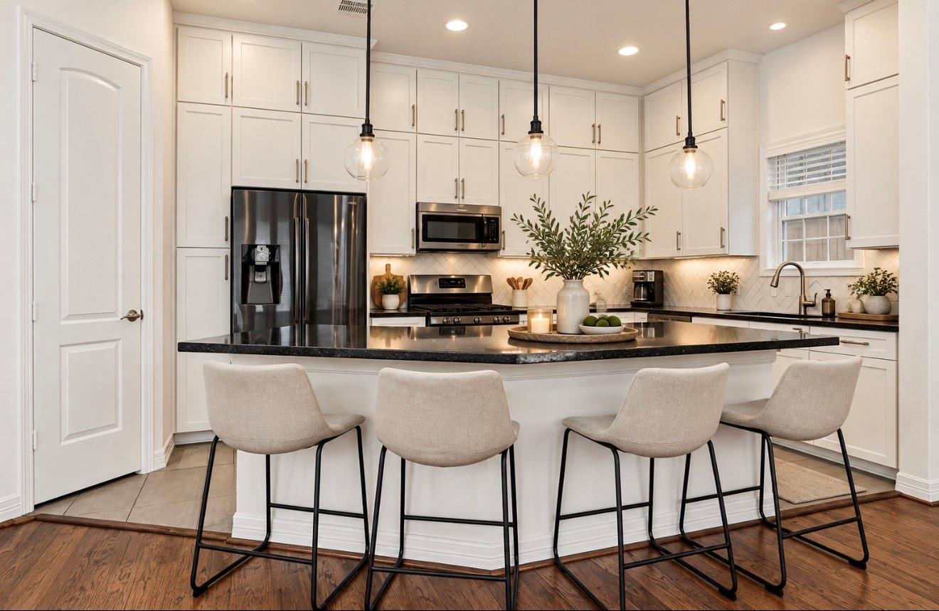 Bright white kitchen with a large island, dark countertops, and four upholstered bar stools.