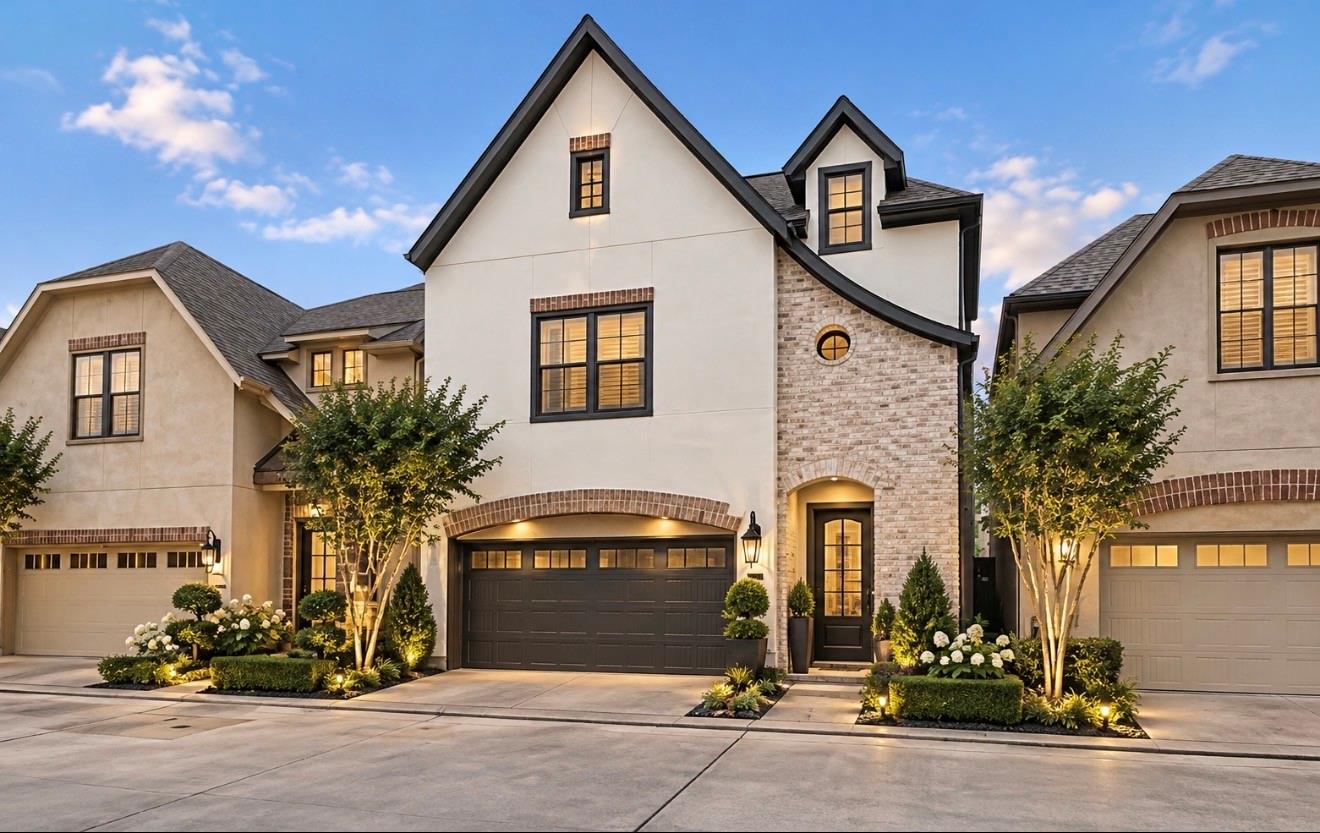 Front of a two-story home with a brick entry, dark garage, and landscaped gardens.