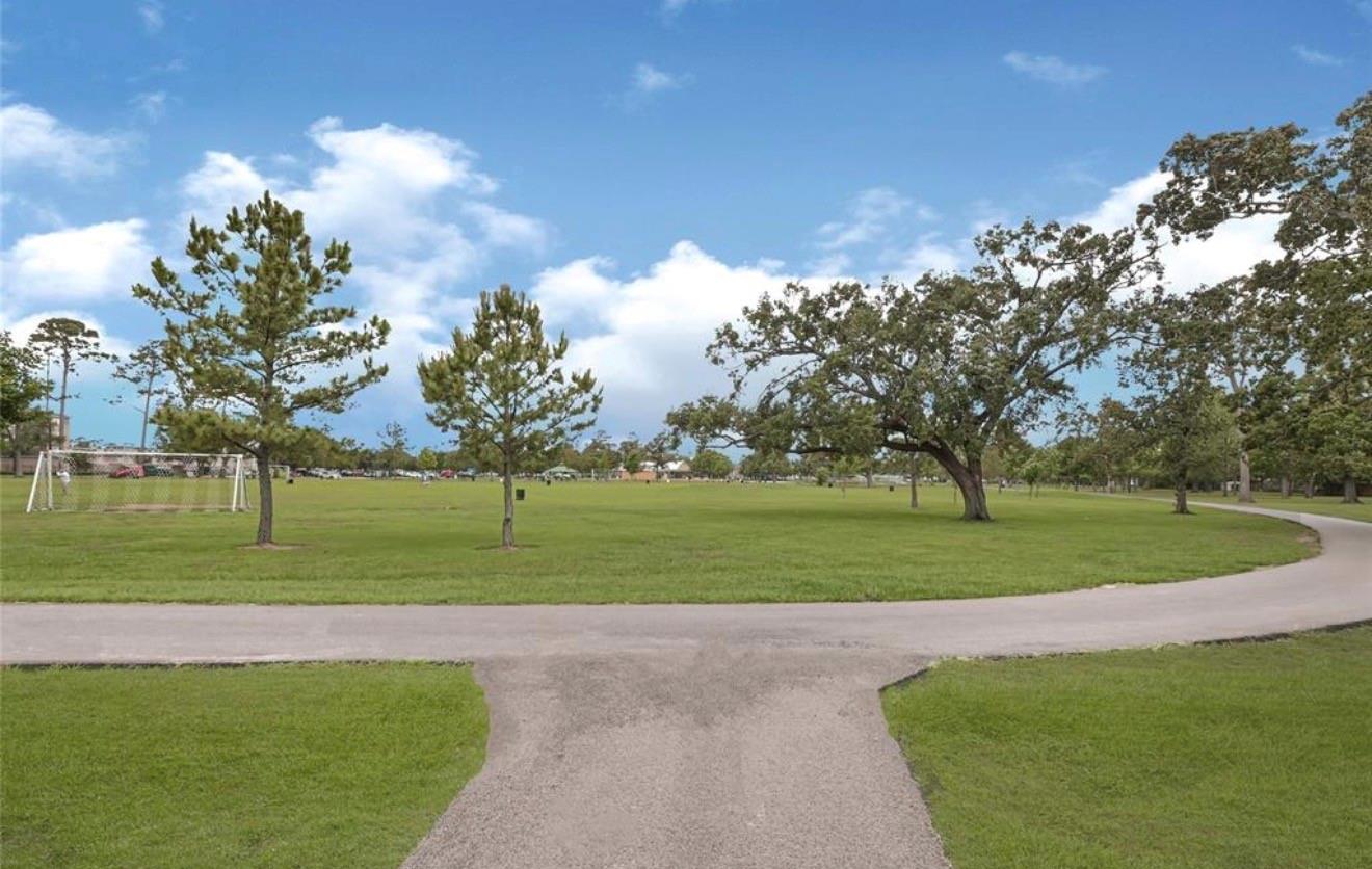 Grassy park with a curving paved path, scattered trees, and a soccer goal.