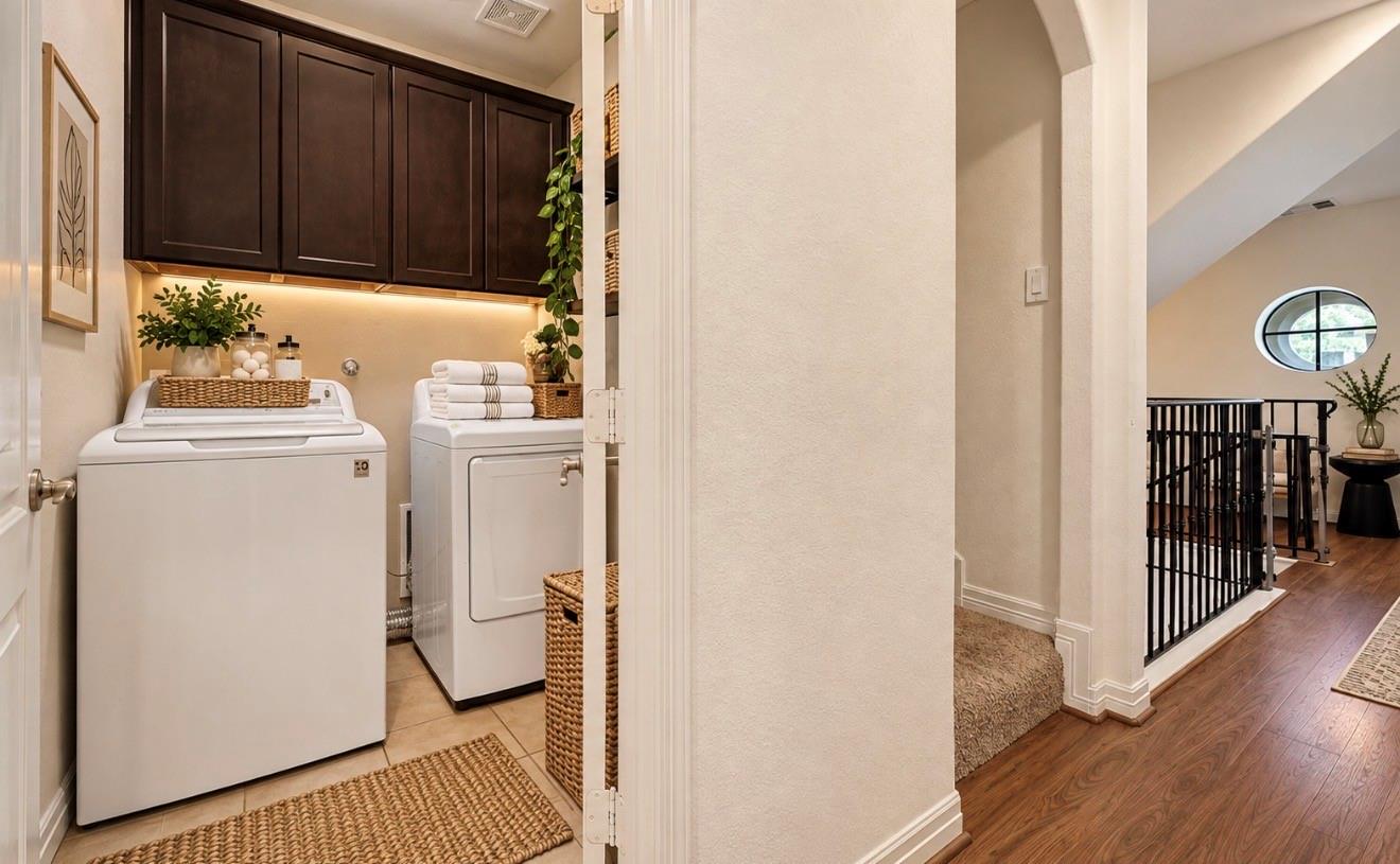 Laundry room with washer and dryer beneath dark cabinets, beside a landing with an oval window.