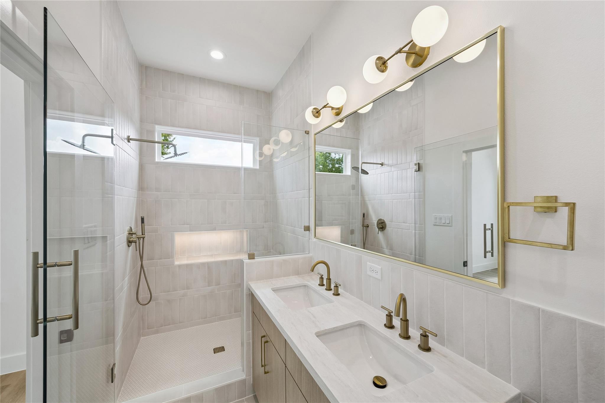 Bright tiled bathroom with a glass walk-in shower, double vanity, and brass fixtures.