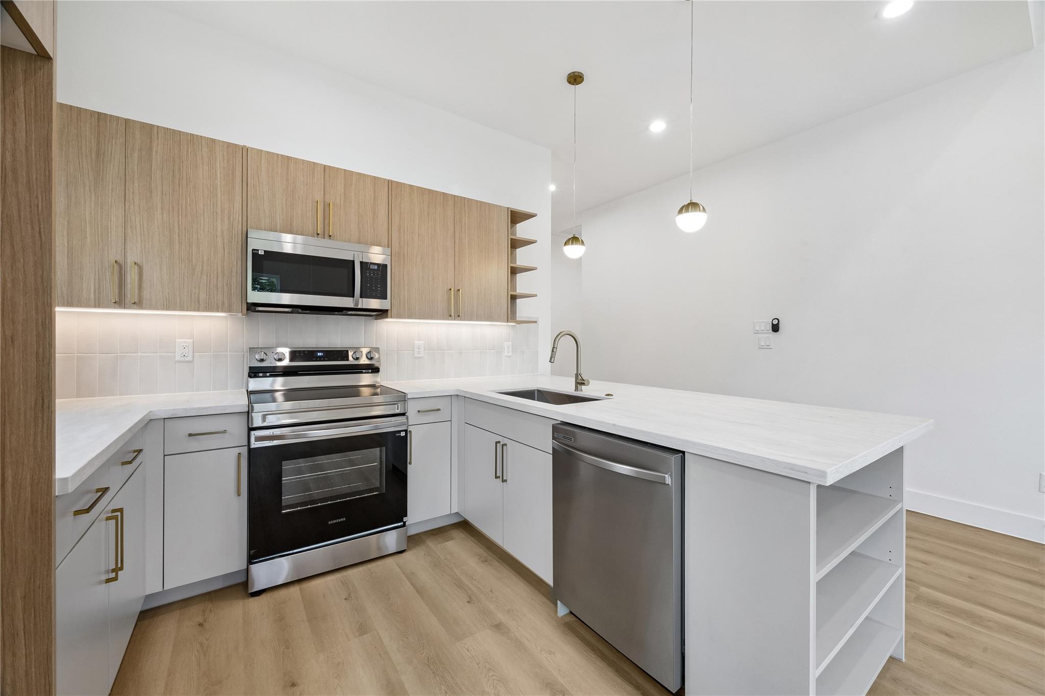 Modern kitchen with wood cabinets, stainless steel appliances, and a broad peninsula with open shelving.