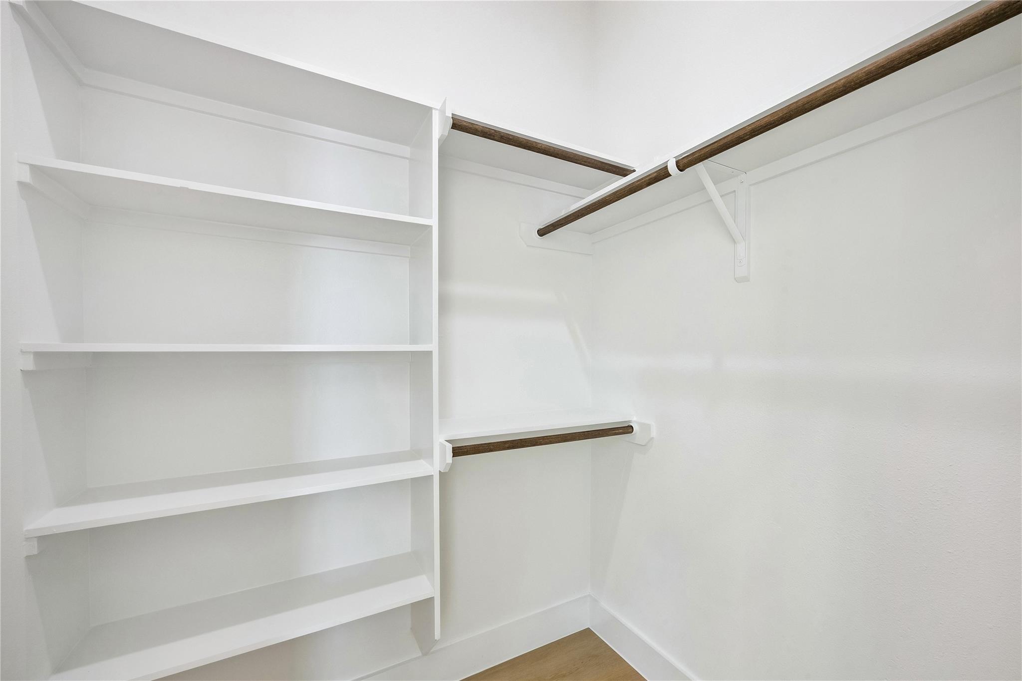 Walk-in closet with white built-in shelves and dark wood hanging rods.