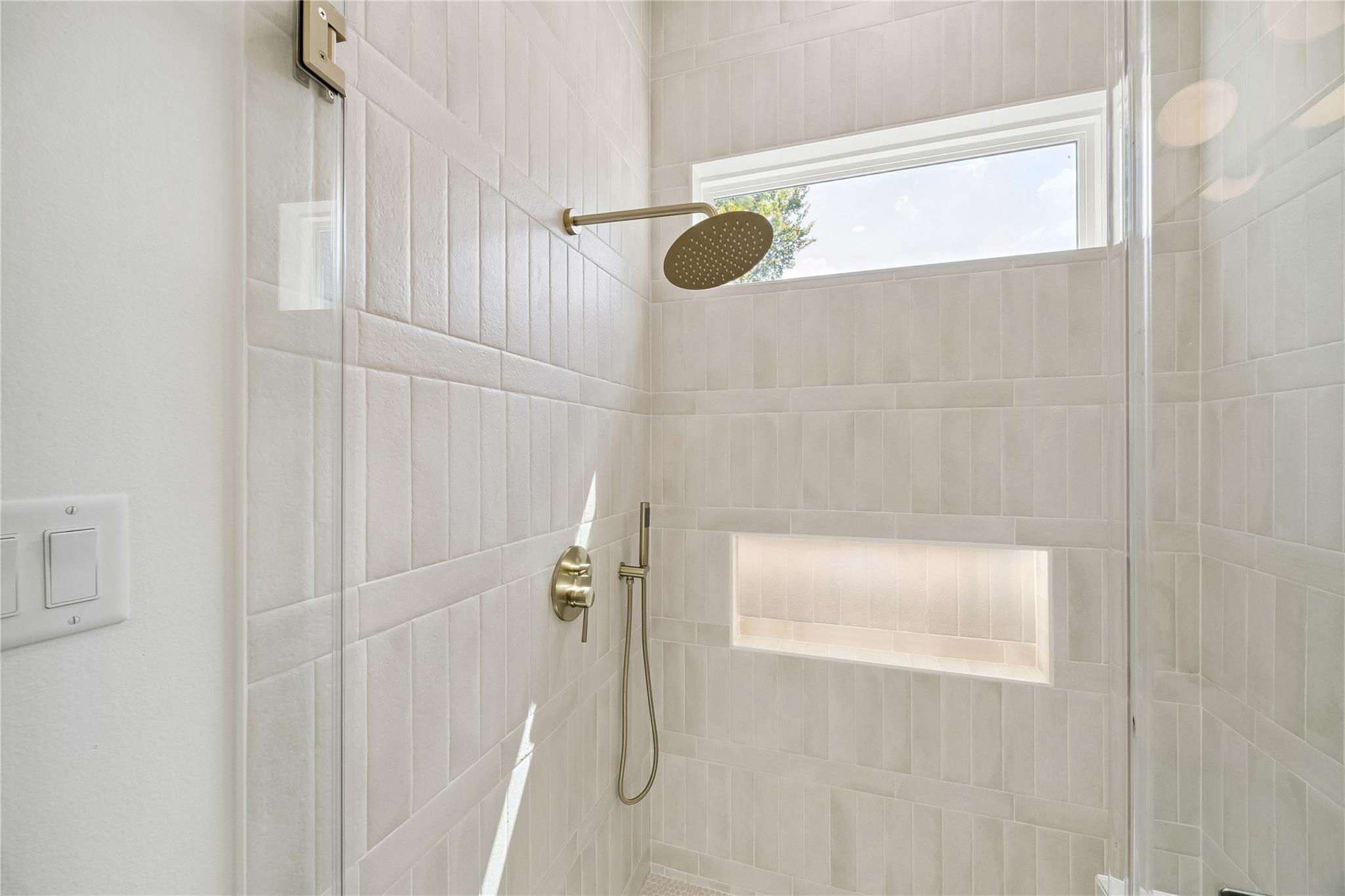 Tiled walk-in shower with brass fixtures, a recessed niche, and a high window.