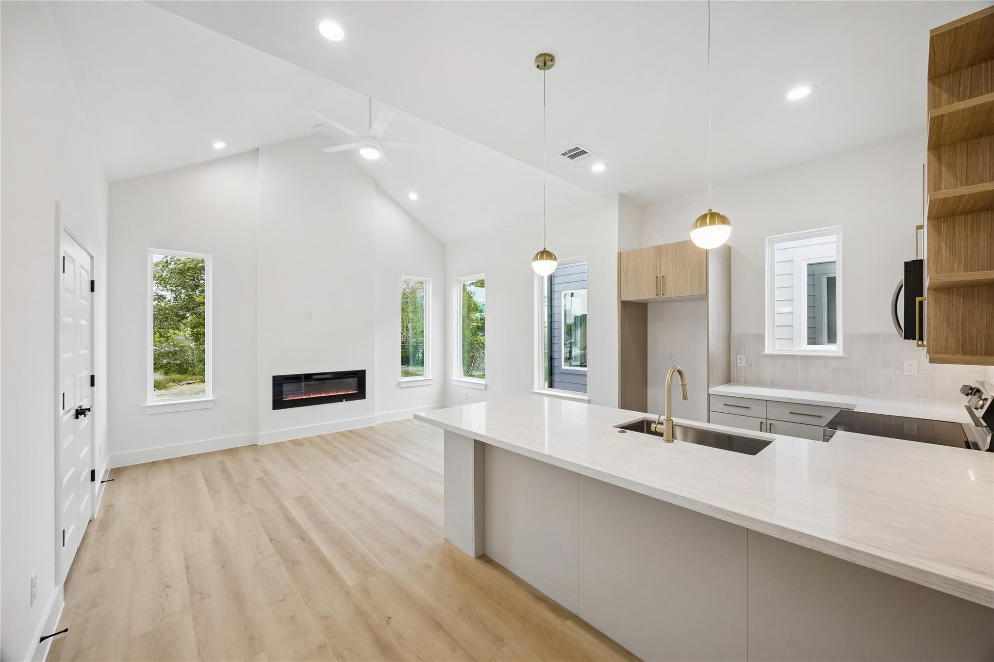Open-plan kitchen and living area with a vaulted ceiling, island, and linear fireplace.