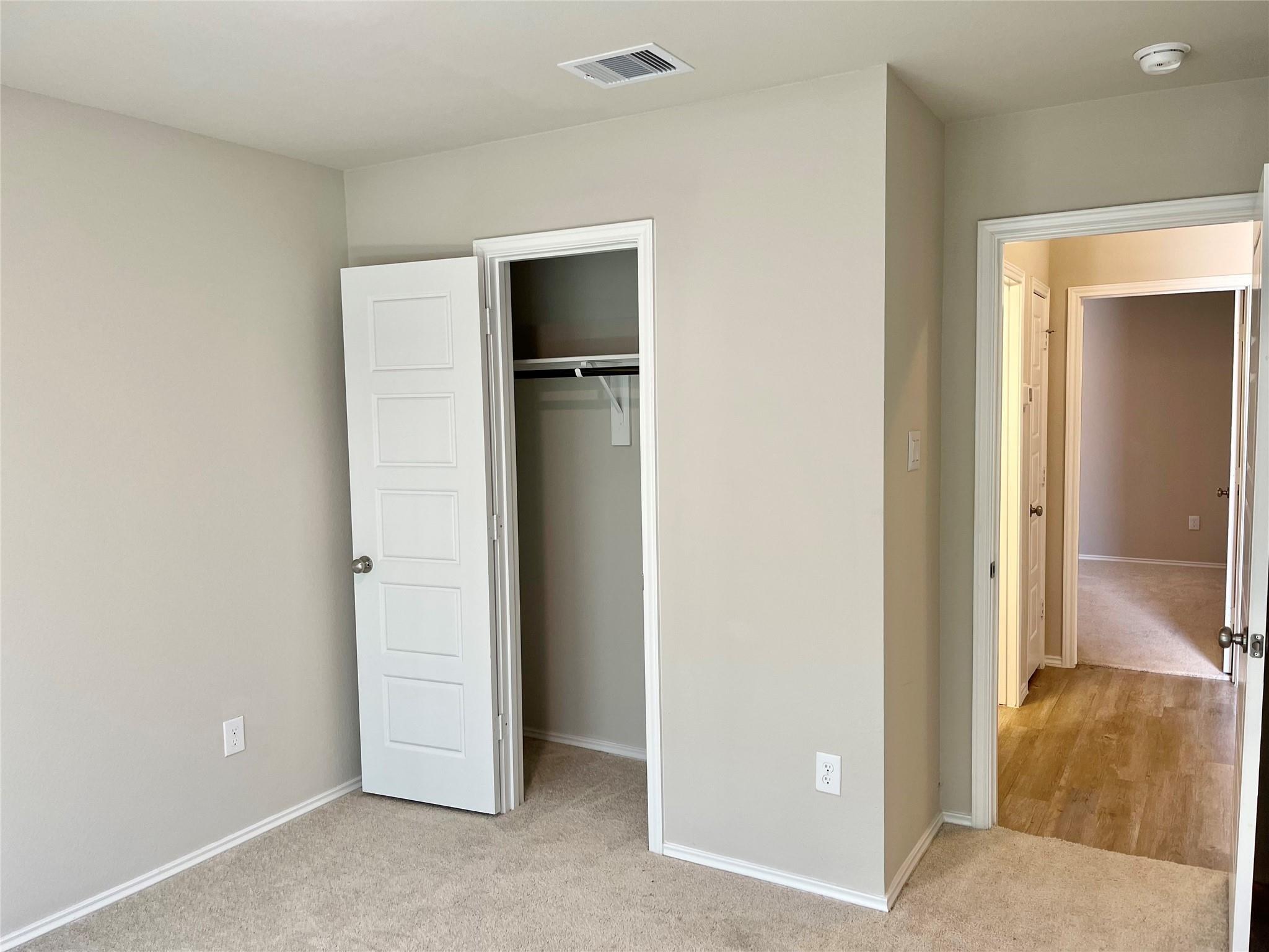 Empty carpeted bedroom with an open closet and a doorway to the hall.