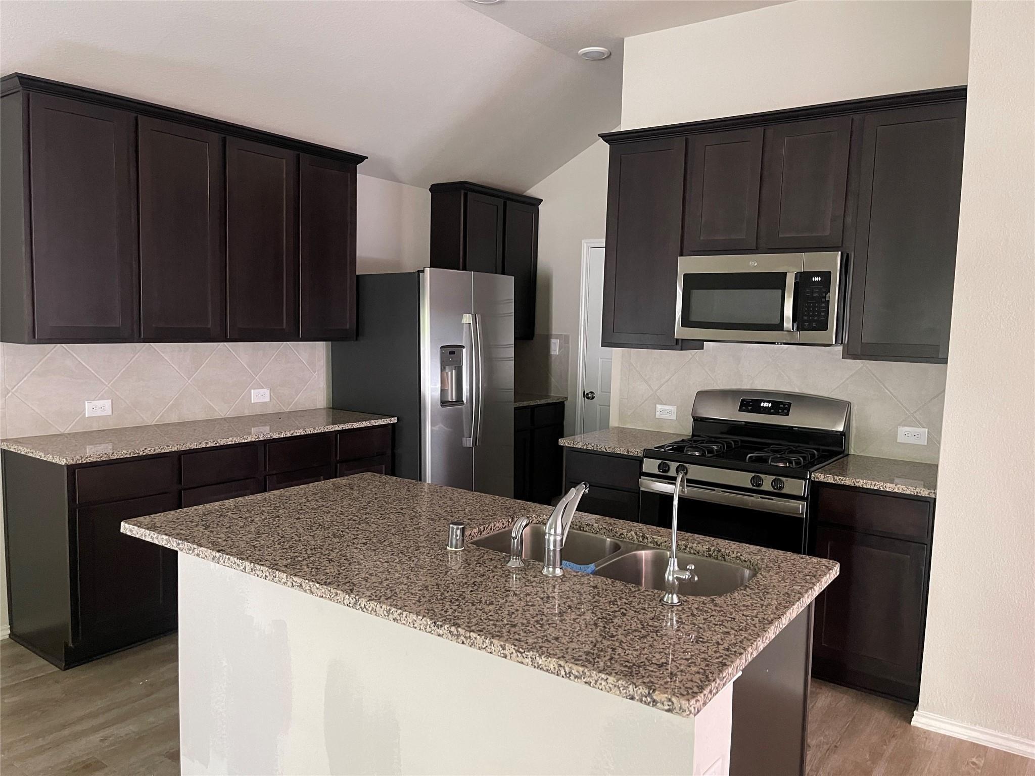 Kitchen with dark cabinets, granite island and stainless steel appliances.