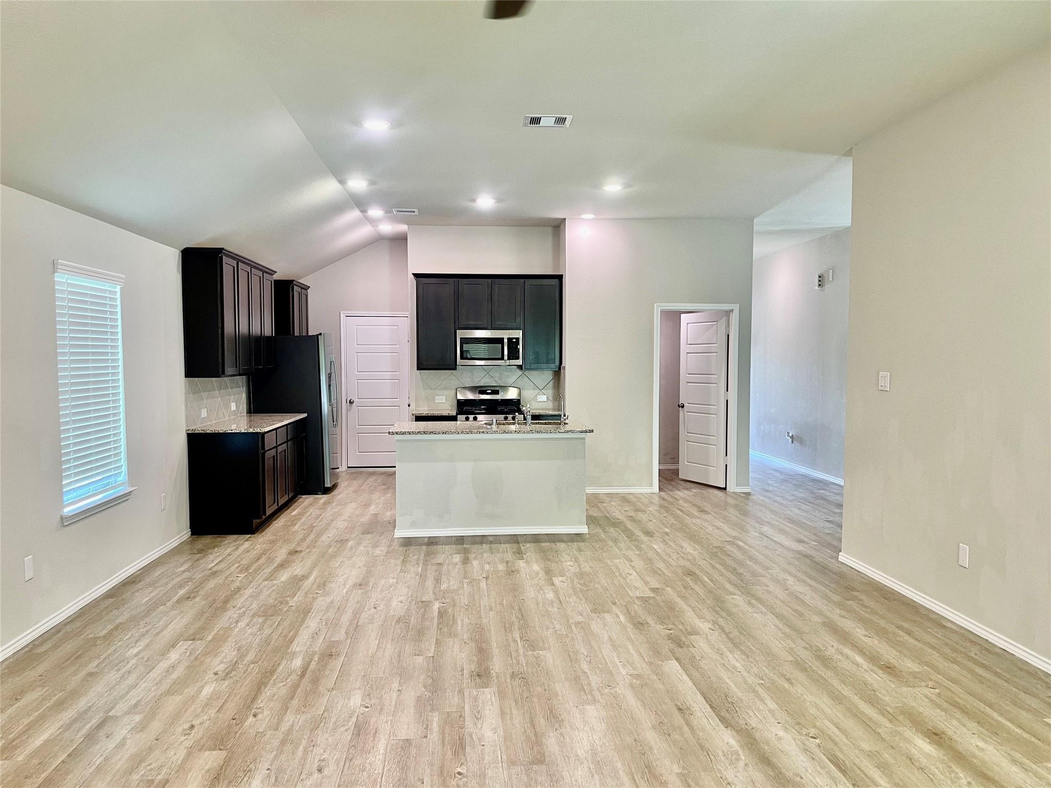 Unfurnished kitchen with dark cabinets, stainless appliances, a peninsula, and wood-look flooring.