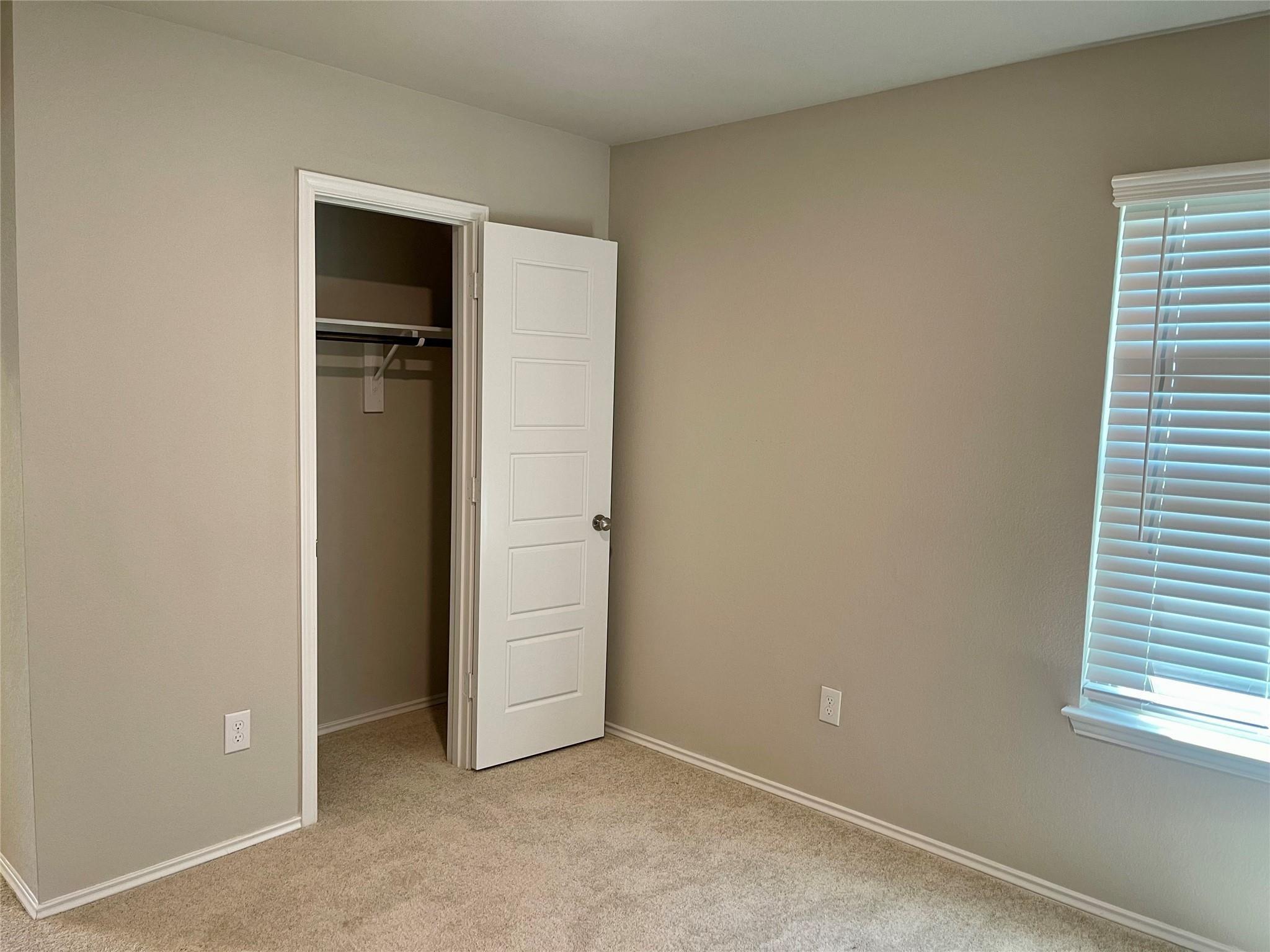 Empty carpeted bedroom with an open closet and a window with white blinds.