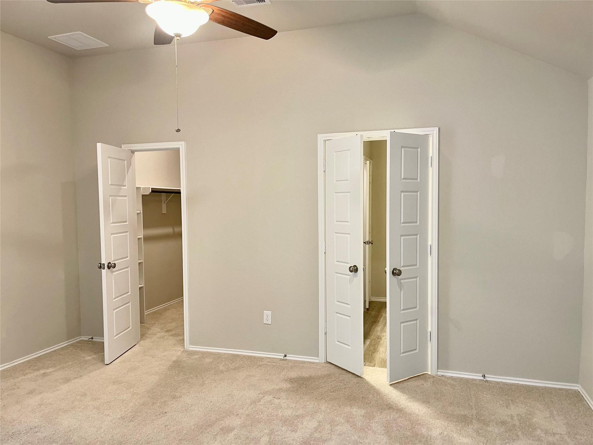 Empty carpeted bedroom with a ceiling fan and two open doorways.