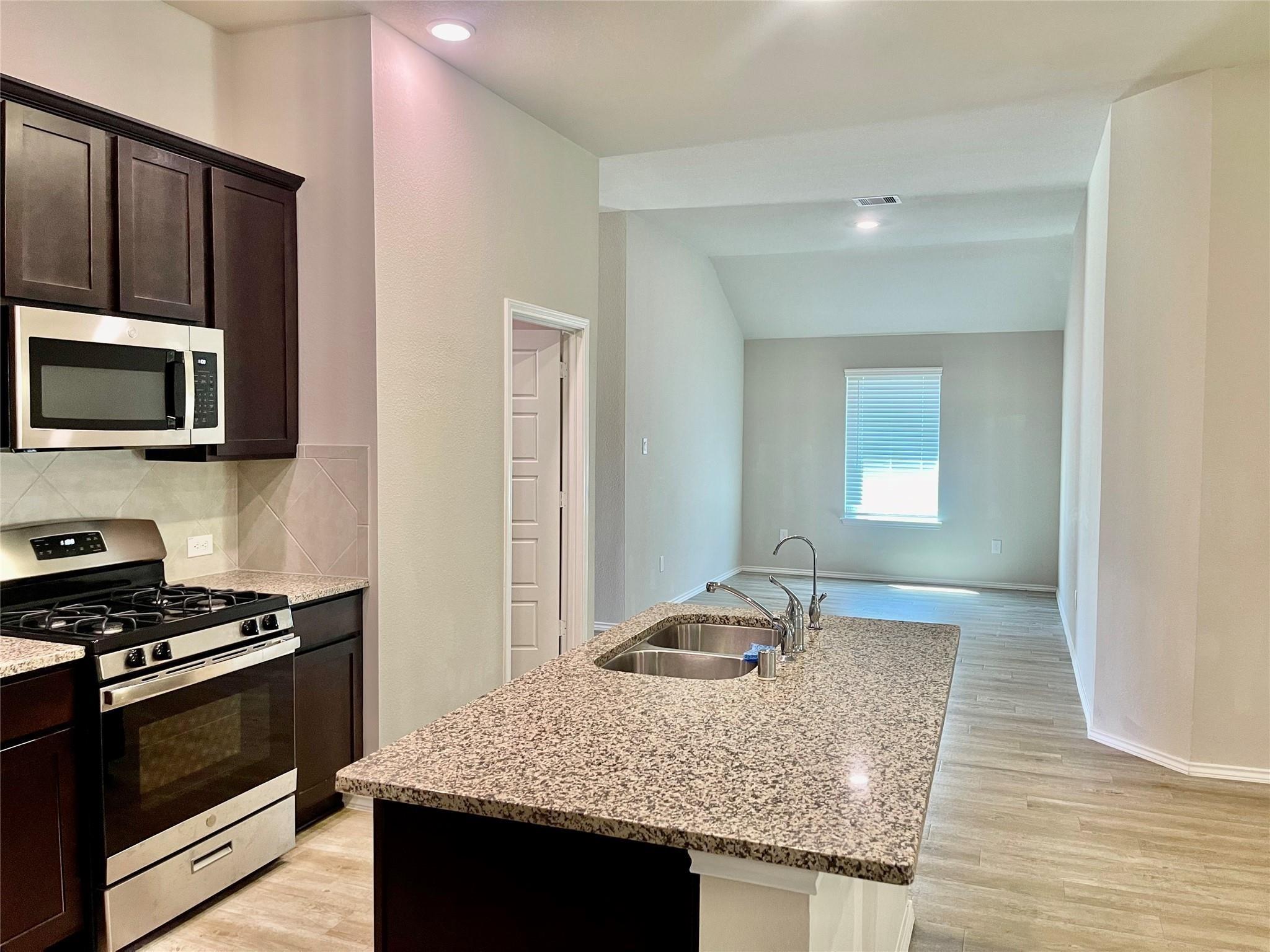 Kitchen with a large granite island and dark cabinets, opening to an unfurnished room.