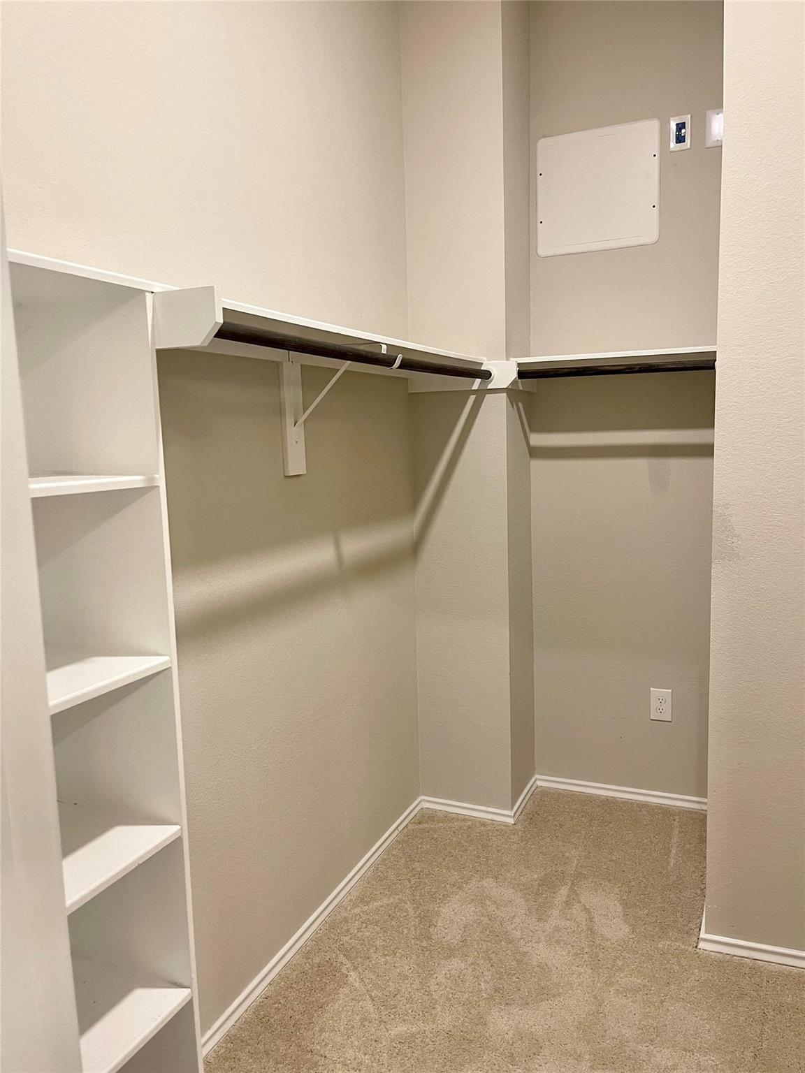 Walk-in closet with built-in shelving, hanging rods, and beige carpet.