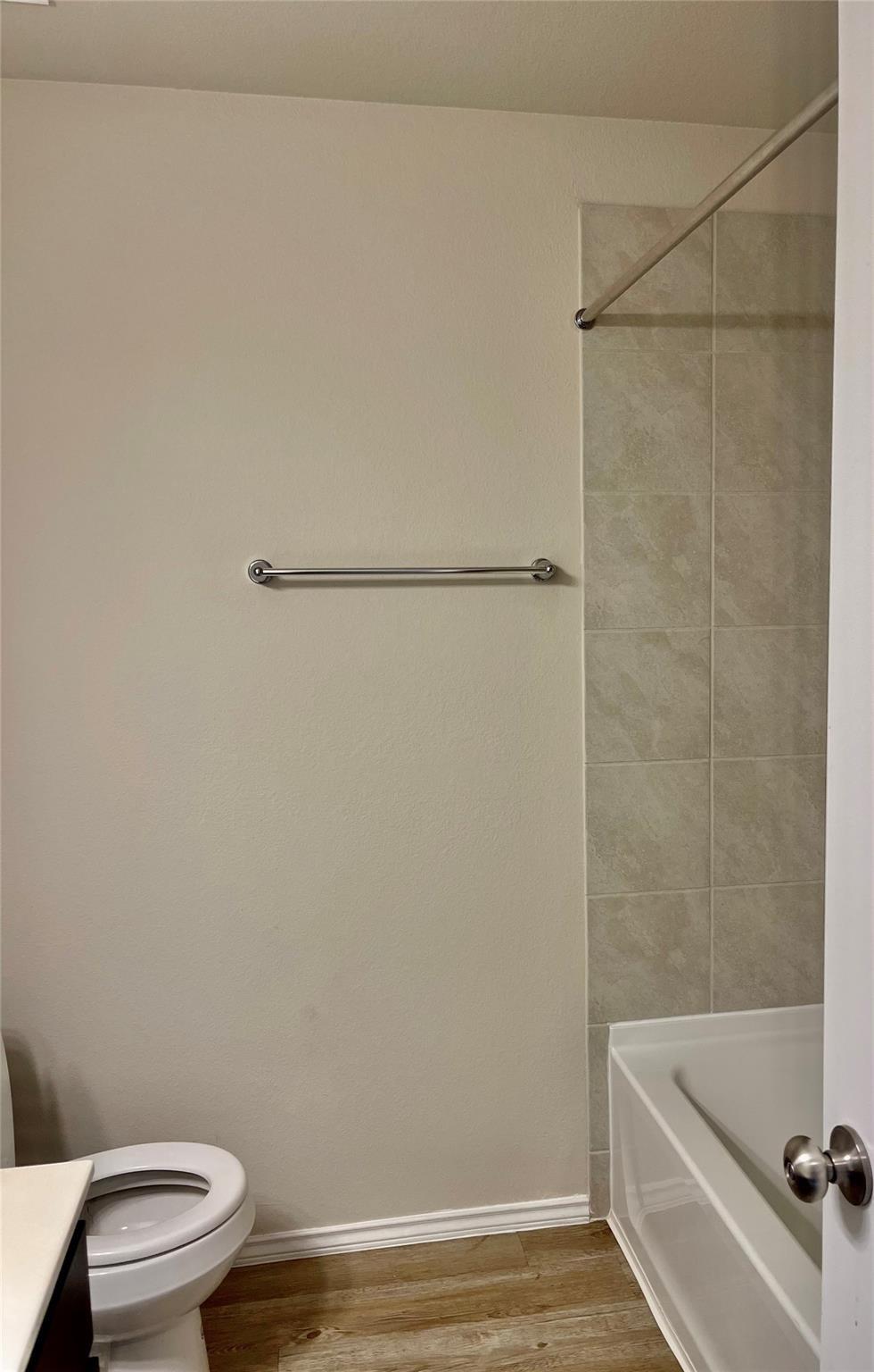 Bathroom with a white tub, tiled surround, and wood-look flooring.