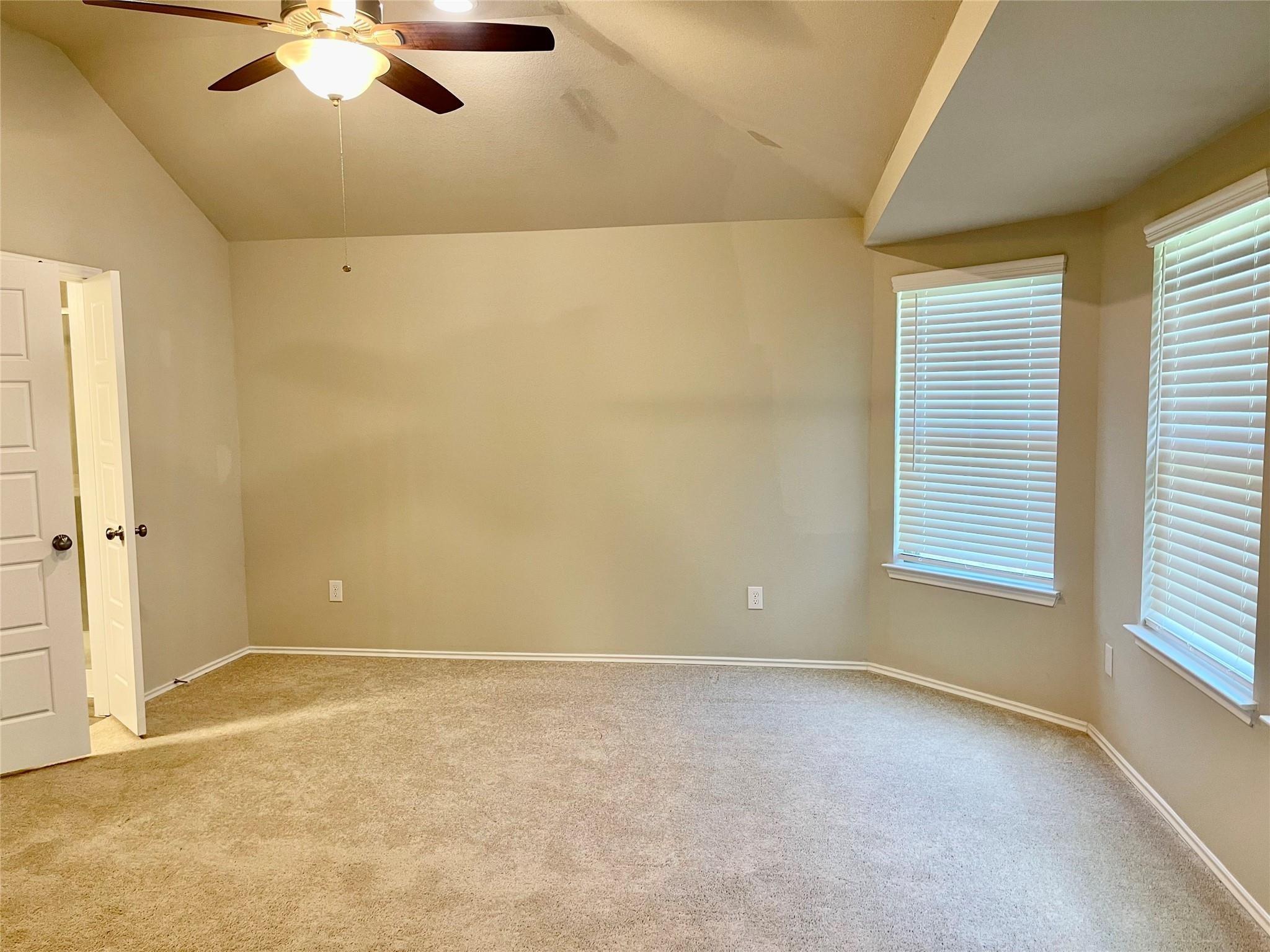 Empty carpeted bedroom with two windows and a ceiling fan with light.