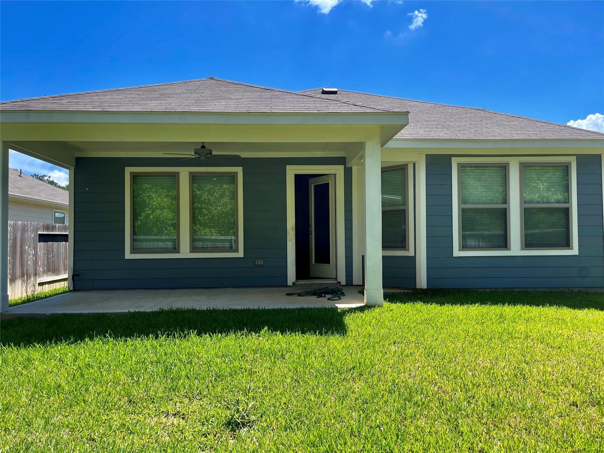 Blue-gray house with a covered patio and broad green lawn.