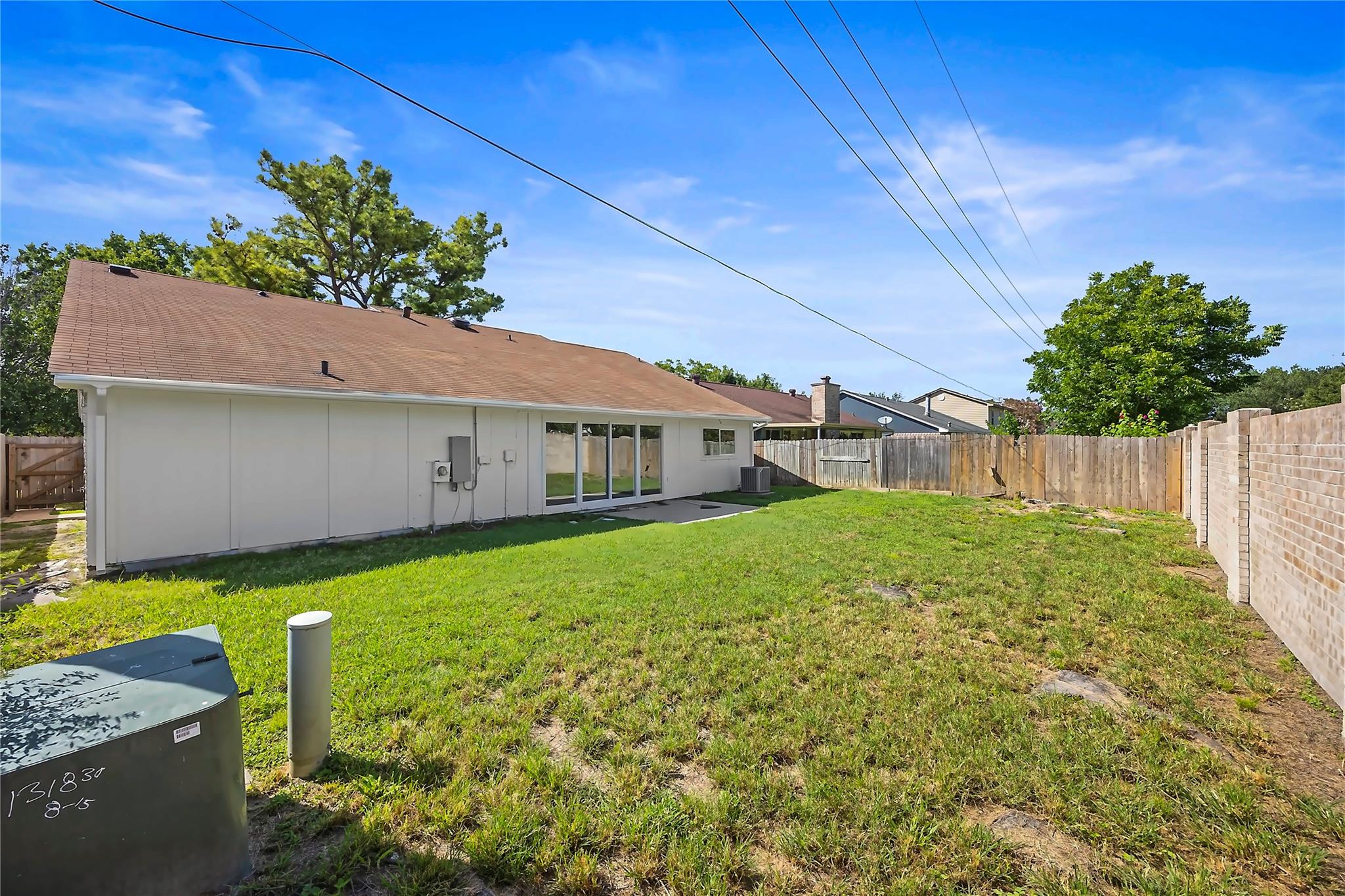Rear of a single-story house overlooking a grassy, fenced backyard with sliding glass doors.