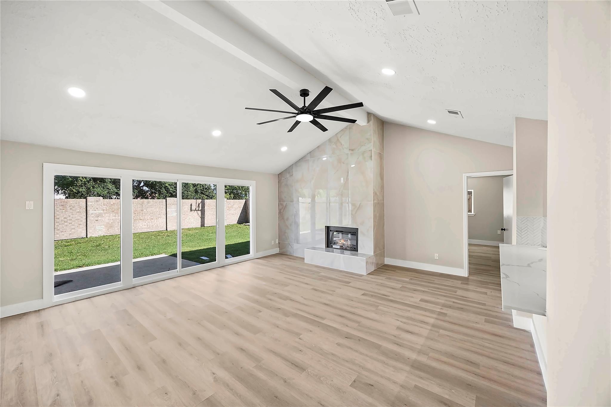 Unfurnished living room with a tiled fireplace, vaulted ceiling, and sliding doors to a fenced backyard.