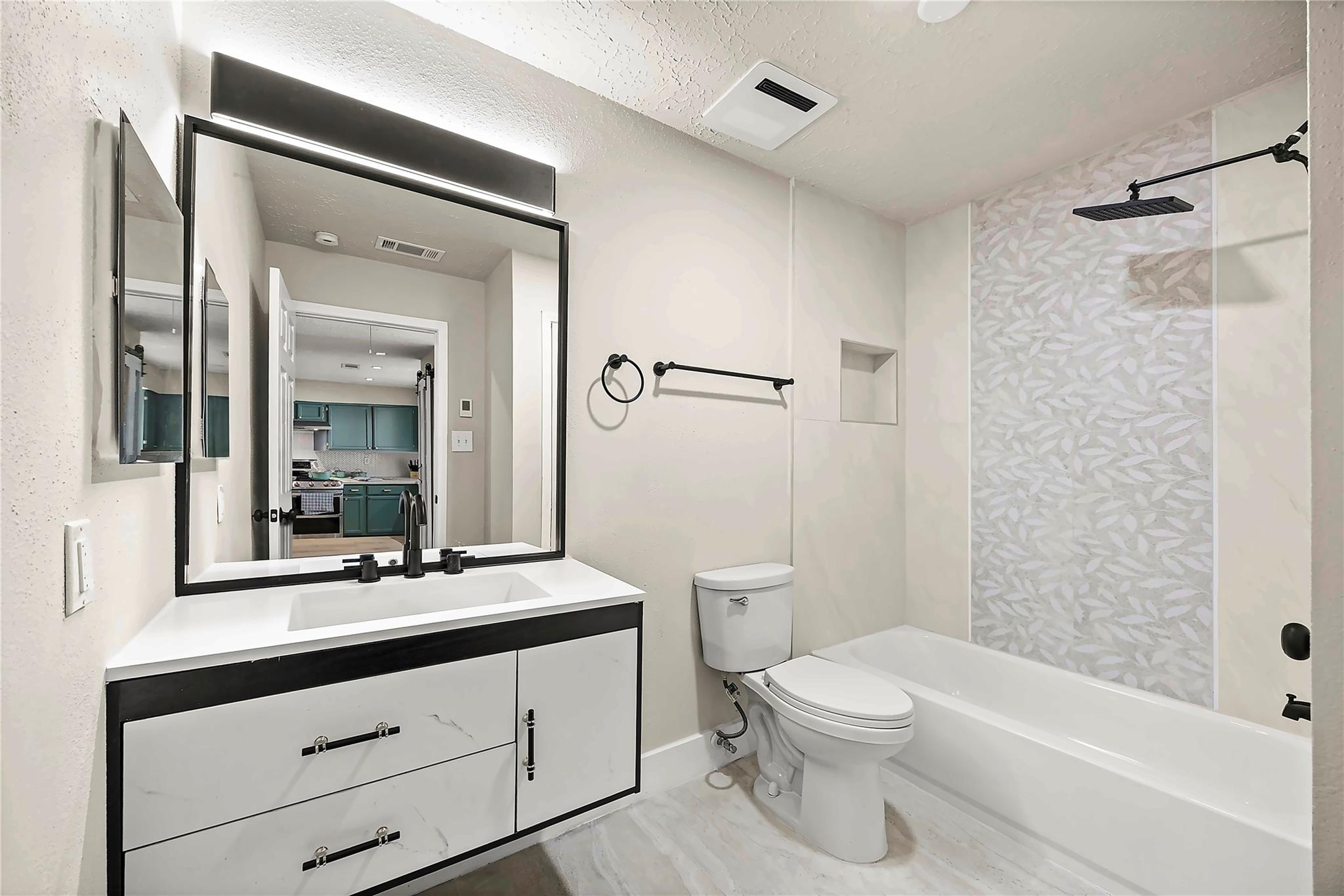 Bathroom with a black-trimmed vanity and mirror, toilet, and bathtub with a patterned shower surround.