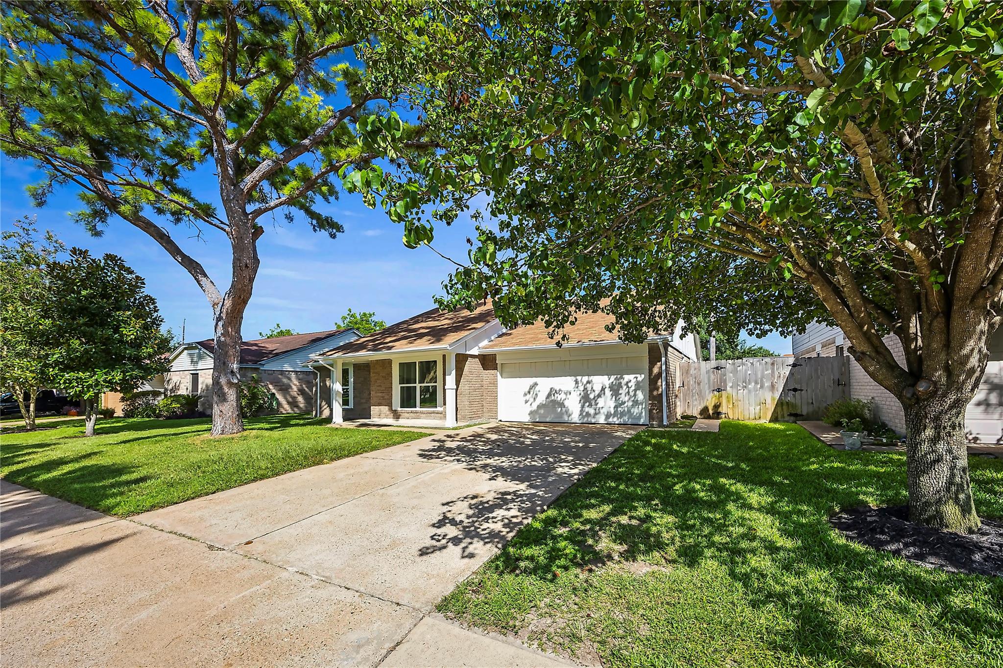 Single-story brick house with a two-car garage, framed by mature trees and a green lawn.