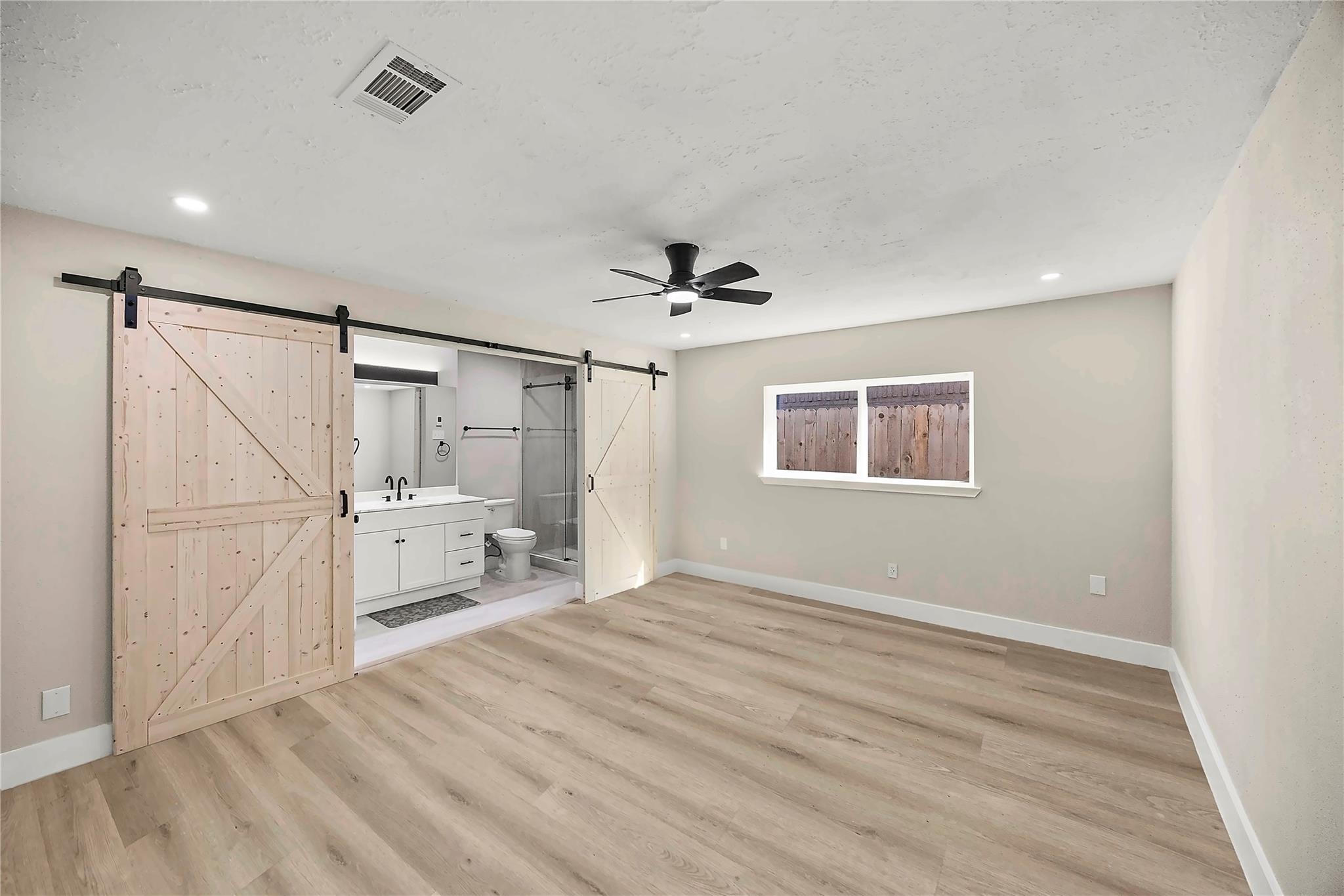 Unfurnished bedroom with sliding barn doors opening to an ensuite bathroom and glass shower.