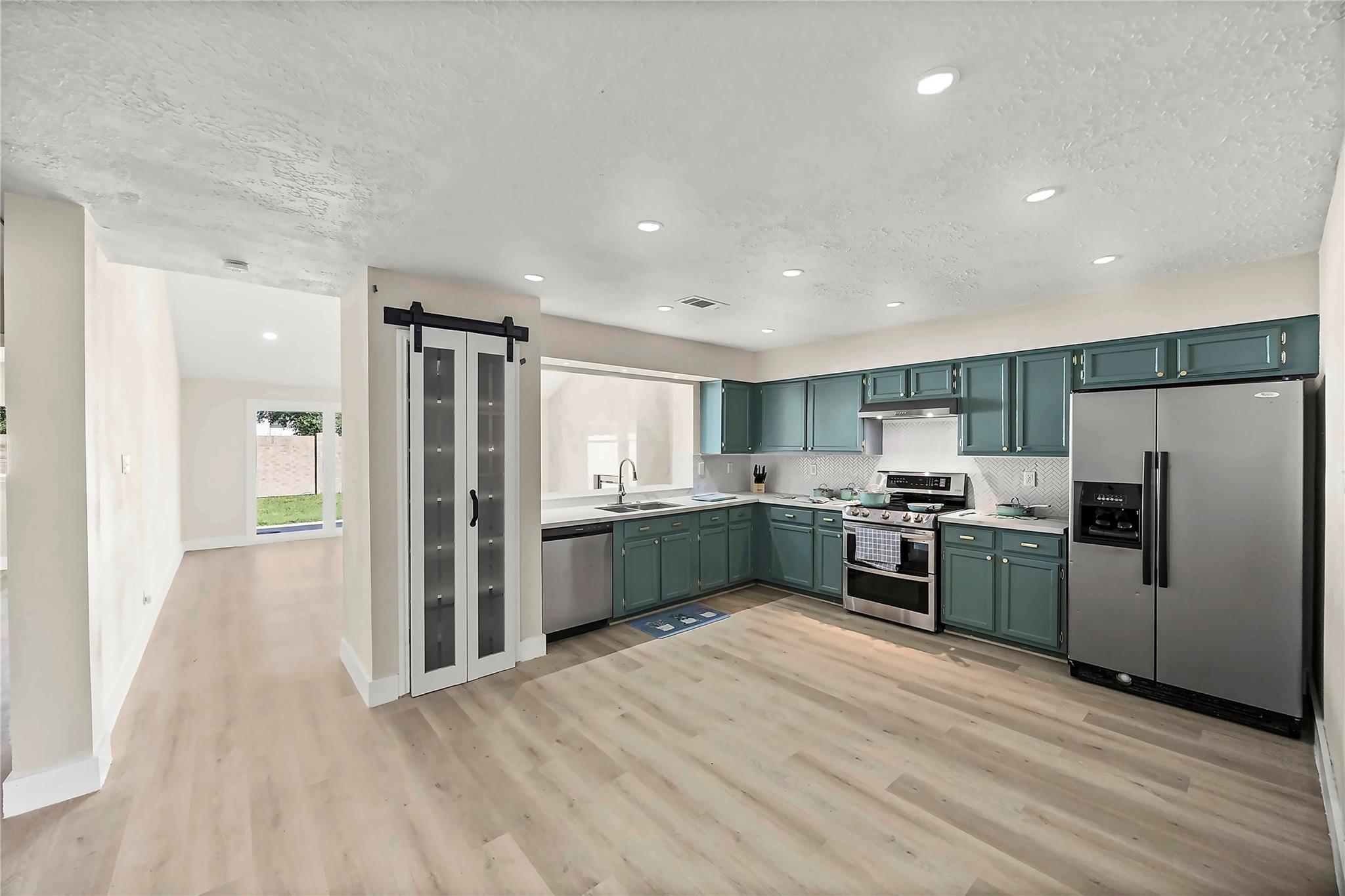 Kitchen with teal cabinets, stainless steel appliances, and a black-trimmed sliding barn door.
