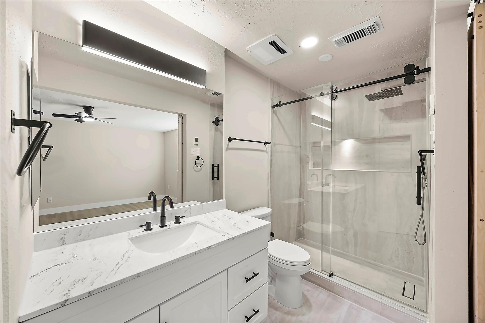 Modern bathroom with a marble-look vanity, black fixtures, and a frameless glass shower.
