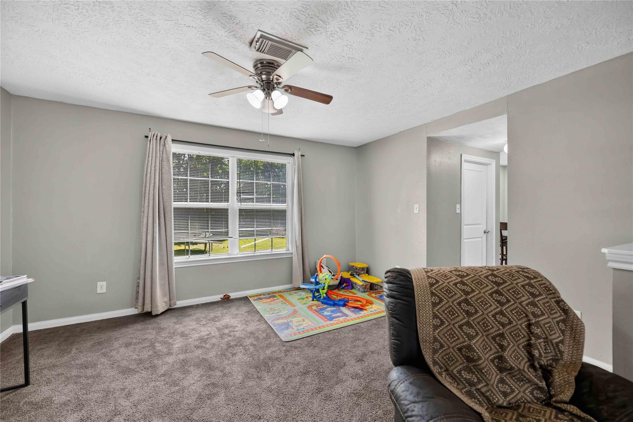 Living room with a carpeted floor, large window, recliner, and children’s play area.