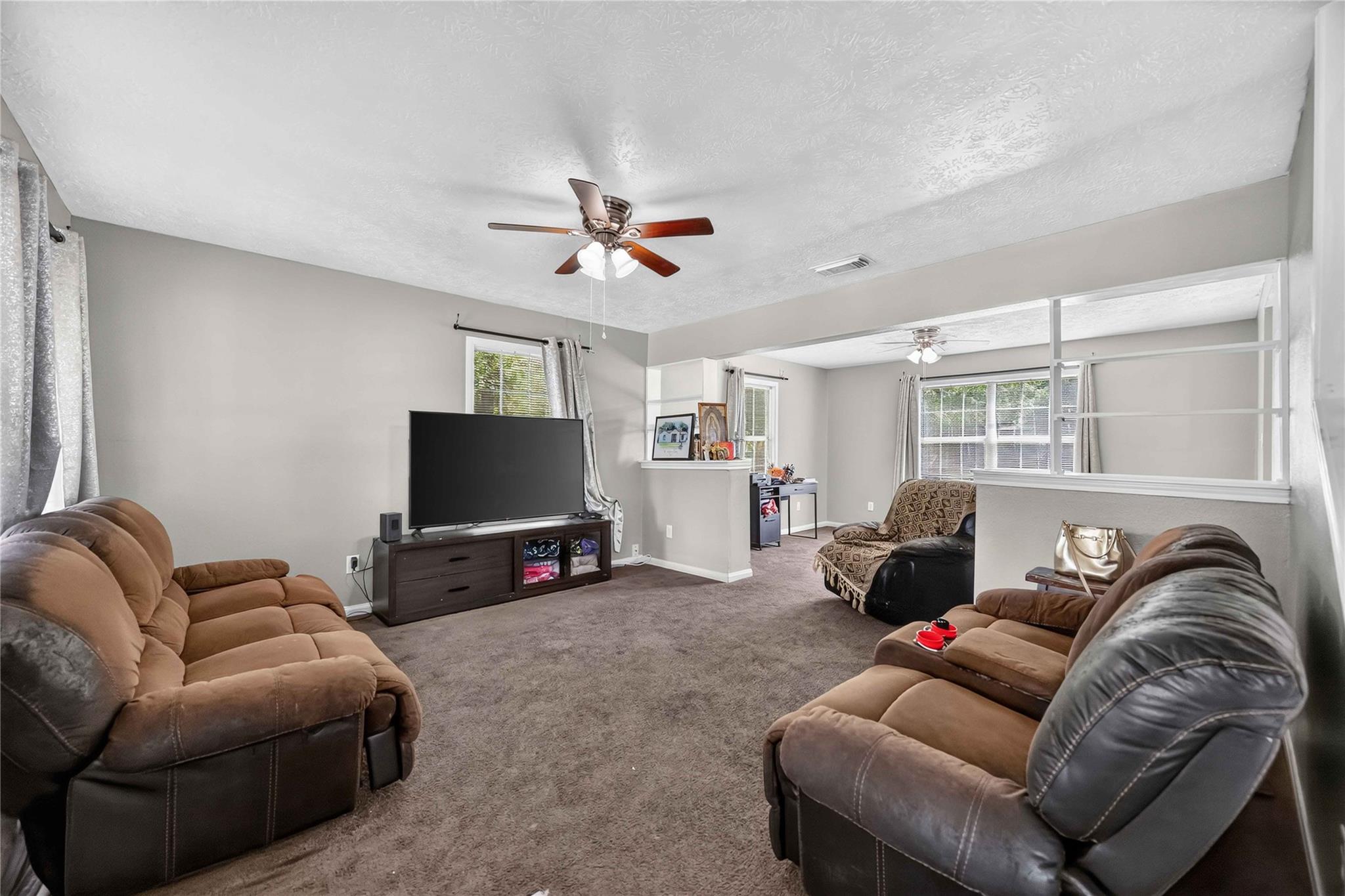 Furnished living room with brown reclining sofas, gray carpet, and a wide interior pass-through.